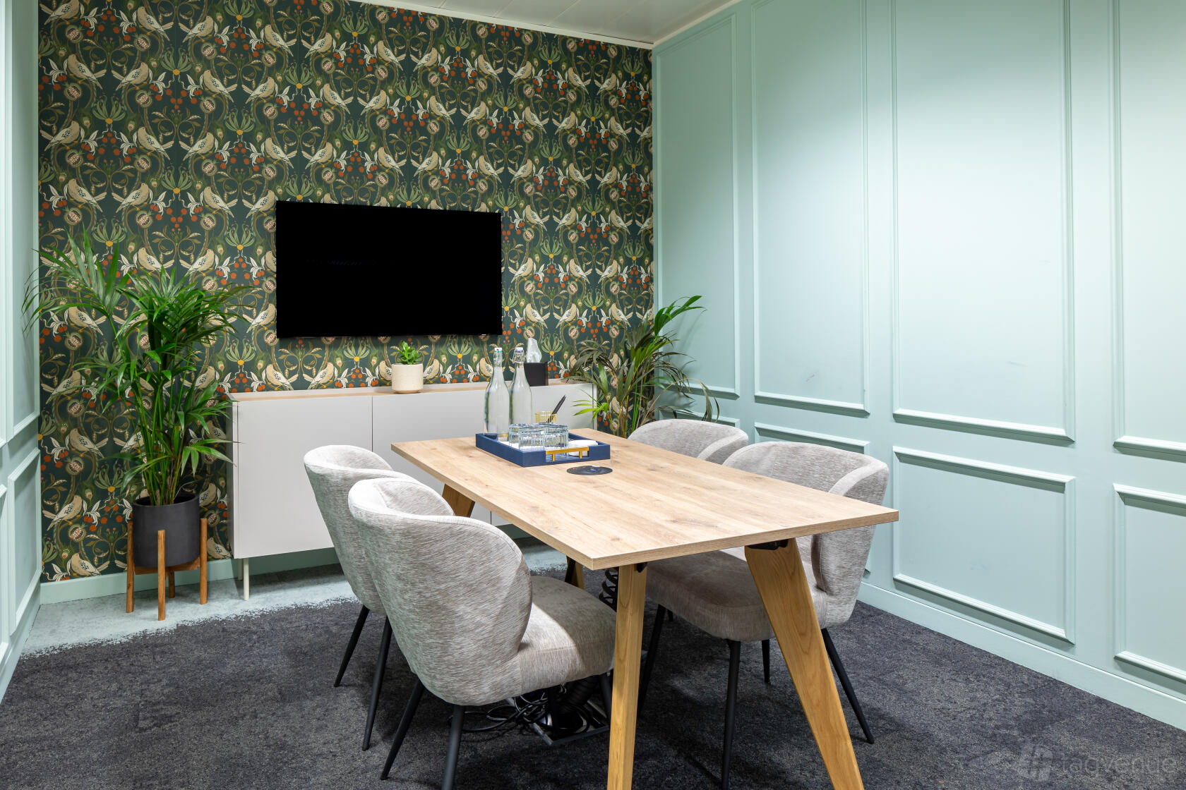 A meeting centre with a wooden table, four upholstered chairs, leafy plants, and a patterned accent wall at Landmark: Cannon Street, London.