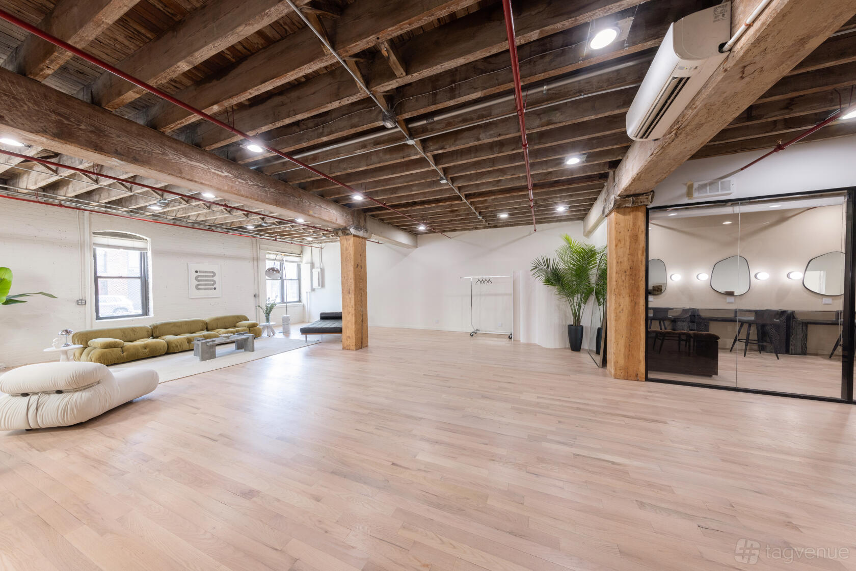A photo and film studio with exposed wooden beams, light wood floors, lounge seating, and glass-walled meeting room at Studios by SK.