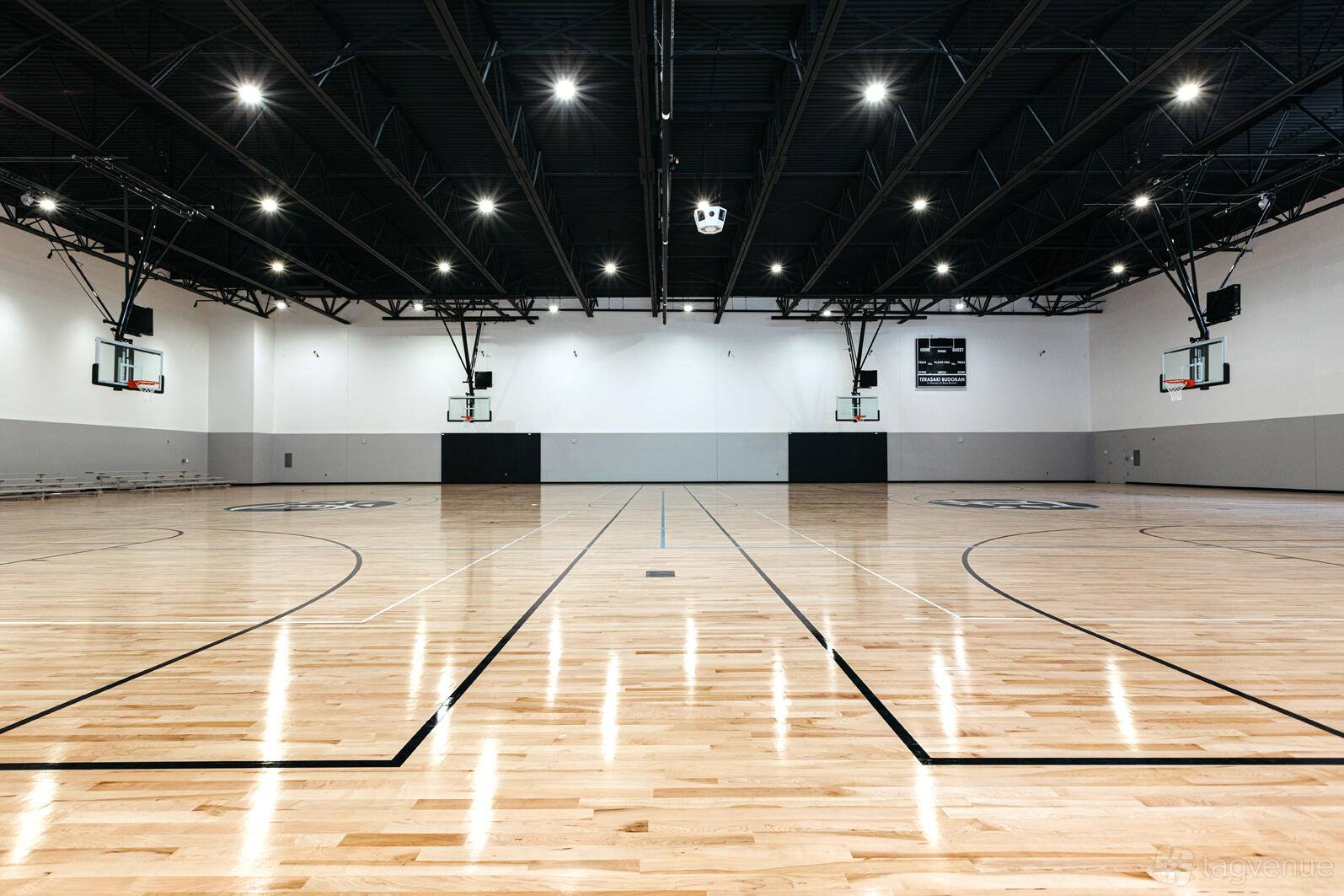 An indoor gymnasium with polished wooden floors, basketball hoops, and bright overhead lighting at Terasaki Budokan.