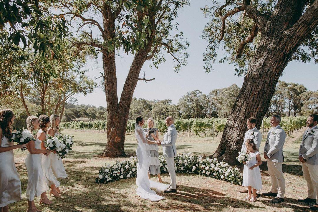 An outdoor space with large shade trees, floral arrangements, and views of vineyards at Rustico At Hay Shed Hill.