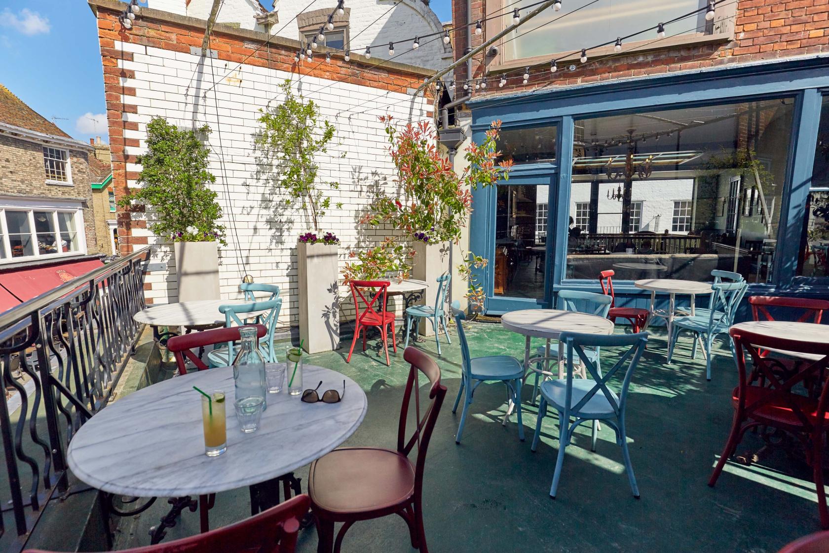 A pub terrace with marble-topped tables, colorful chairs, potted plants, and string lights at The Drapers Arms.