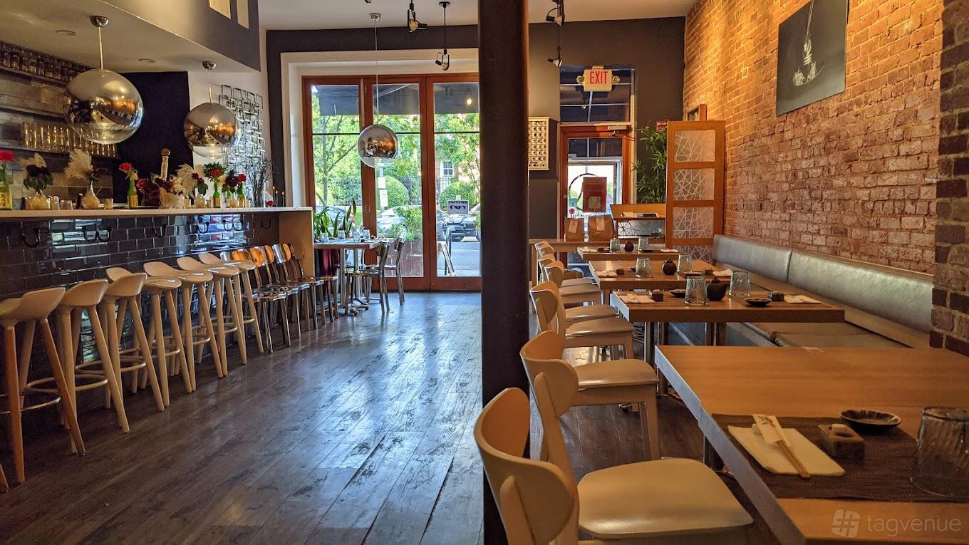 A restaurant with exposed brick walls, wooden floors, glass globe lights, and large front windows at Sushi Hachi.
