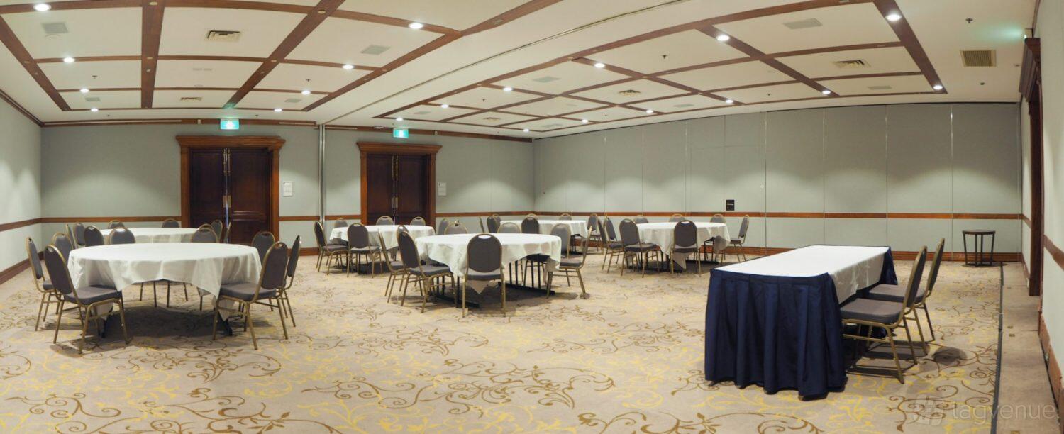 A hotel function room with round tables covered in white linens, gray chairs, and decorative carpet at Fairmont Resort Blue Mountains.