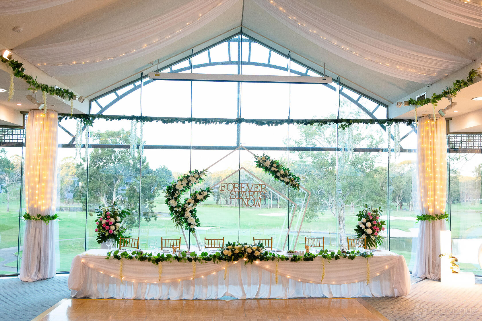A lounge with floor-to-ceiling windows, draped ceilings, floral arrangements, and a long white-clothed table at Riverside Oaks Resort.