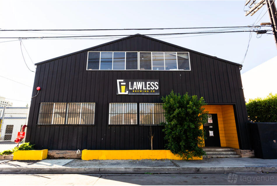 A black warehouse-style brewery exterior with a yellow entryway and large windows at Lawless Brewing Co.