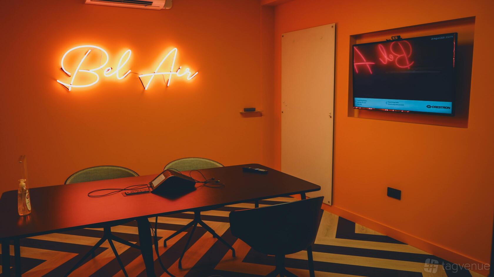A meeting room with a neon 'Bel Air' wall sign, a large screen, and a black conference table at Huckletree Ancoats.