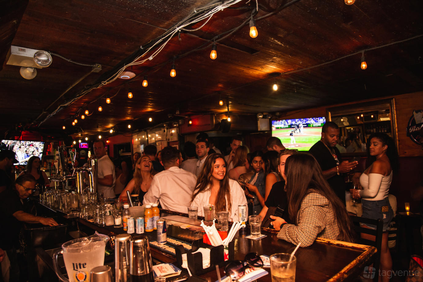 A bar with a long wooden counter, hanging string lights, and TVs displaying sports at The Grisly Pear Midtown.