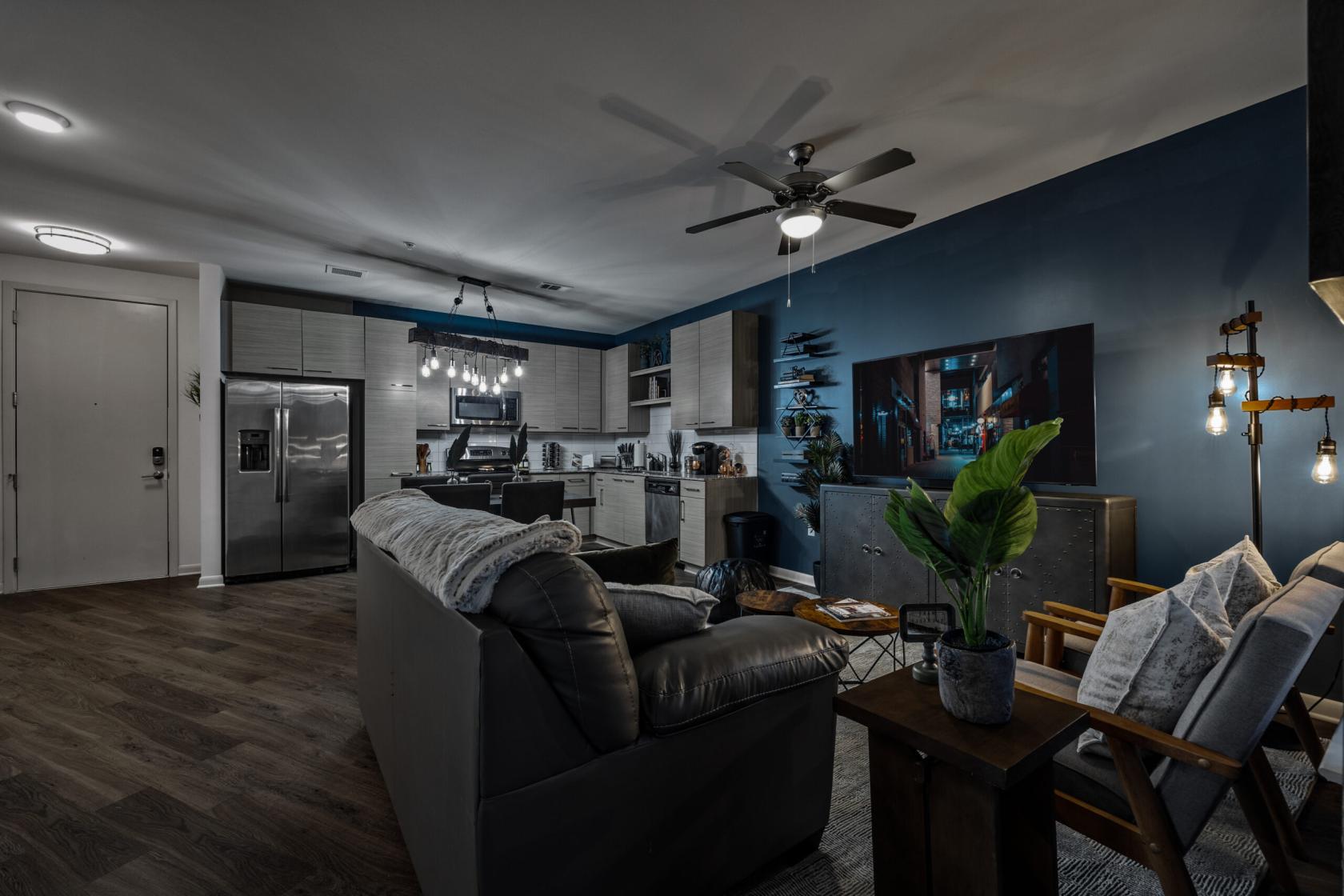 An apartment living area with leather sofa, wood flooring, dark blue accent wall, and open kitchen at 'Industrial Chic' Apartment.