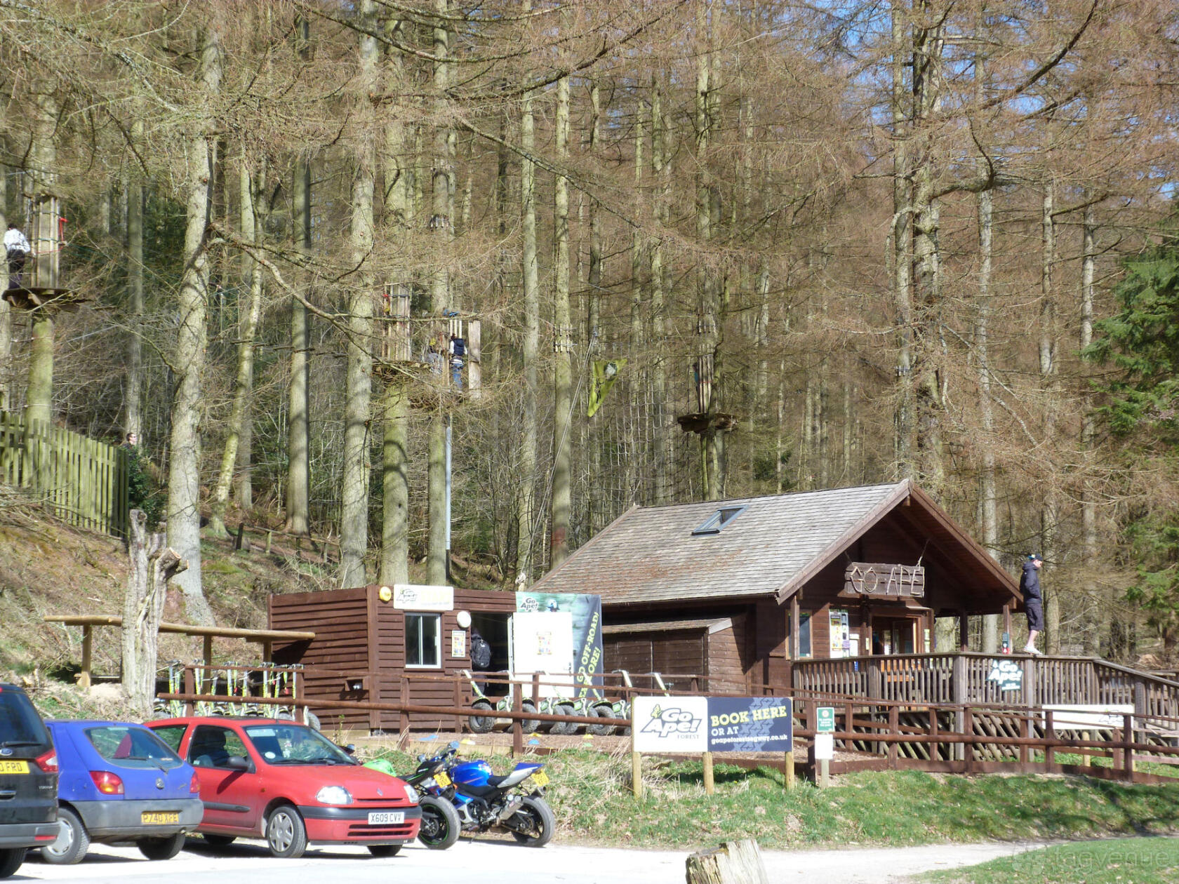An outdoor adventure venue with a wooden lodge, raised deck, and treetop rope platforms at Go Ape Dalby.