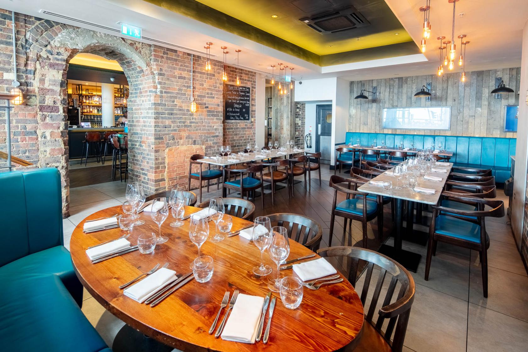 A dining room with exposed brick archways, wood-paneled walls, and long tables set with glassware at The Salt Room.
