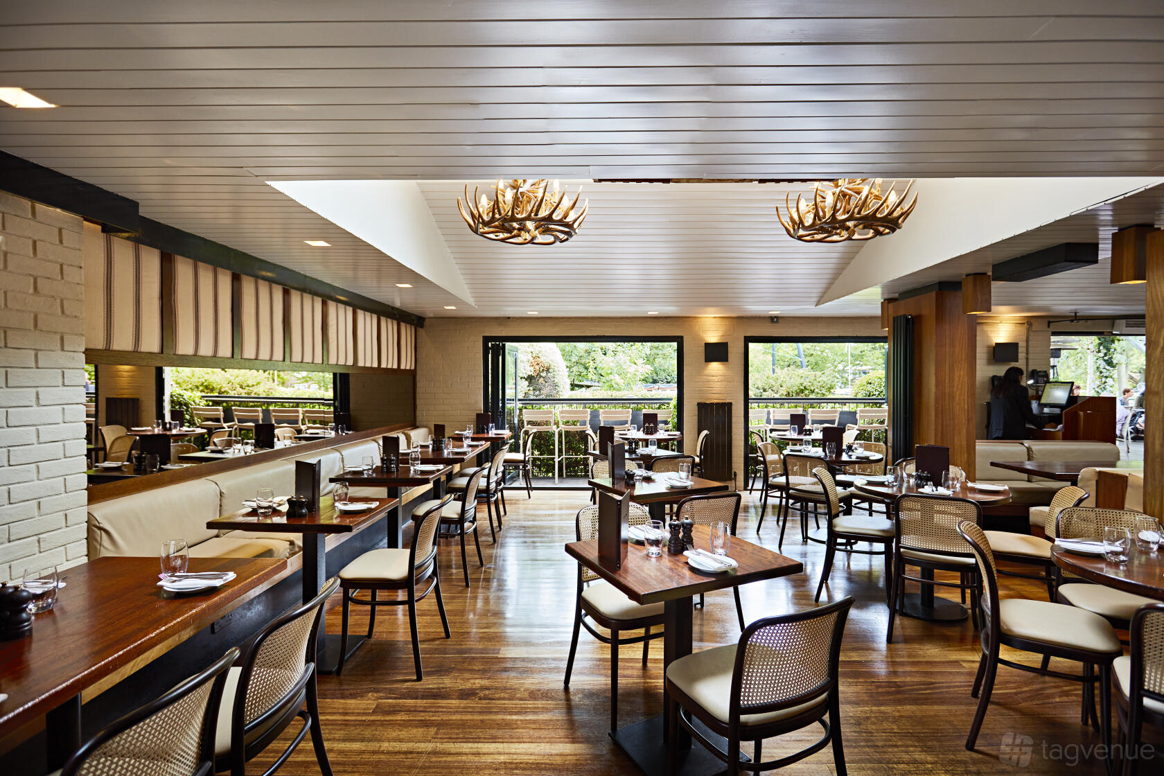 A restaurant with large windows, wooden floors, light brick walls, and antler-shaped ceiling lights at The Waterway.