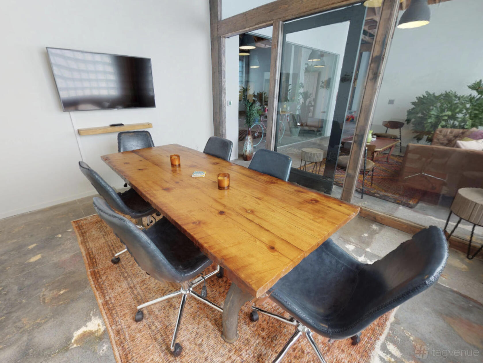 A meeting room with a wooden conference table, black chairs, wall-mounted TV, and glass walls at Unita Hermosa Beach.