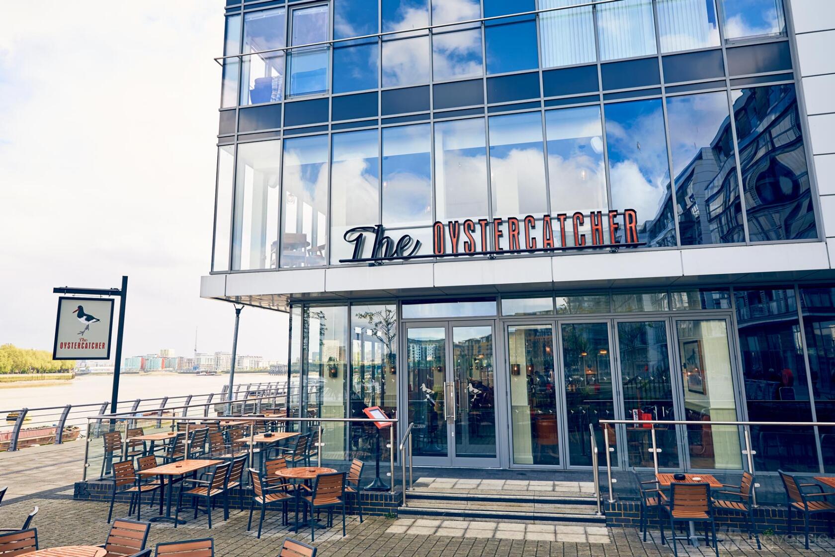 A bar with floor-to-ceiling windows, outdoor seating, and riverside views at The Oystercatcher.