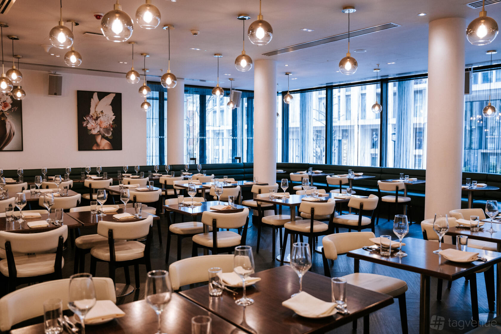A bar dining area with large windows, globe pendant lights, and neatly set wooden tables at The Westminster Bar & Grill.