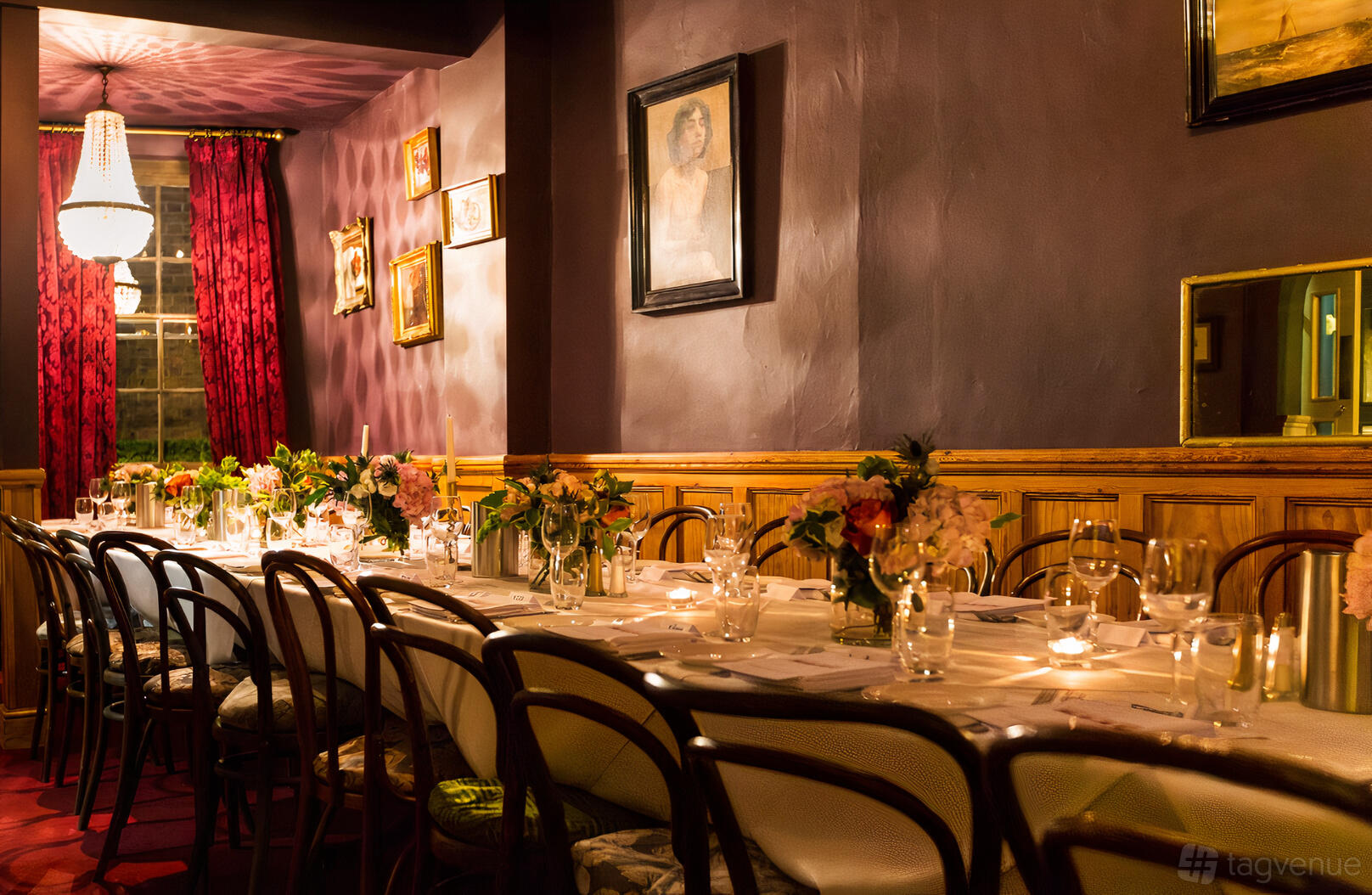 A dining room with a long table set with floral centerpieces, candlelight, and artwork on deep purple walls at Brydges Place Club.