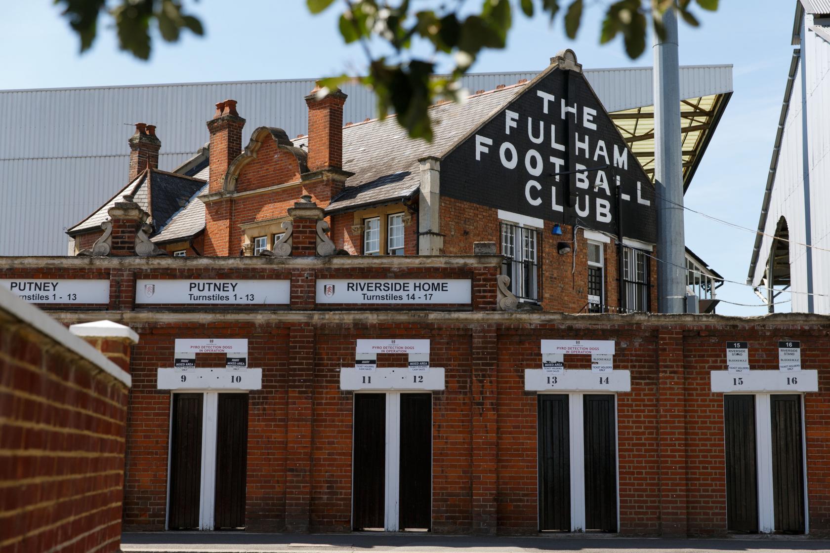 A football stadium entrance with red brick walls, multiple turnstiles, and The Fulham Football Club signage.