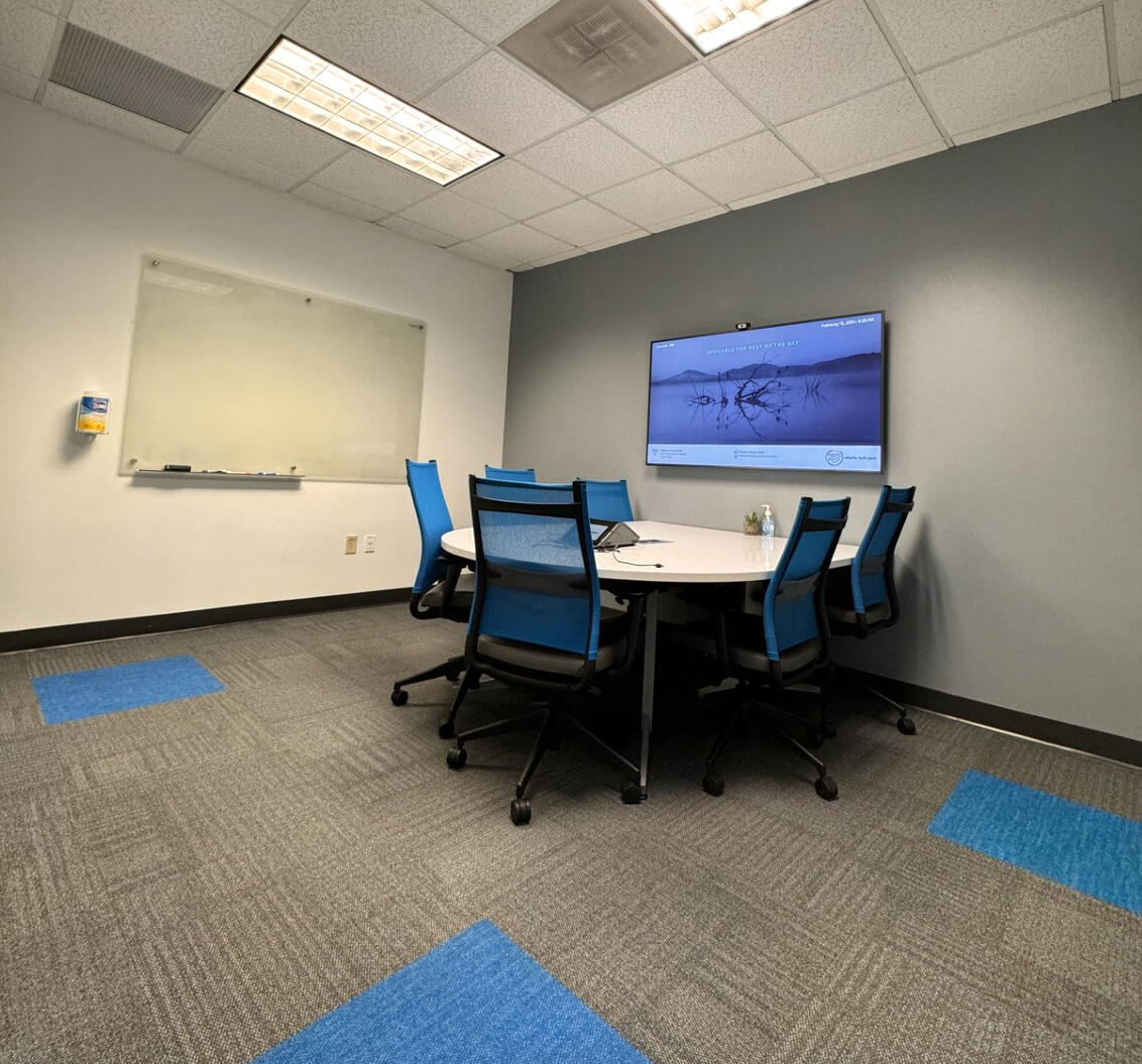 A meeting room with a round table, blue ergonomic chairs, wall-mounted display, and a dry-erase board at Atlanta Tech Park.