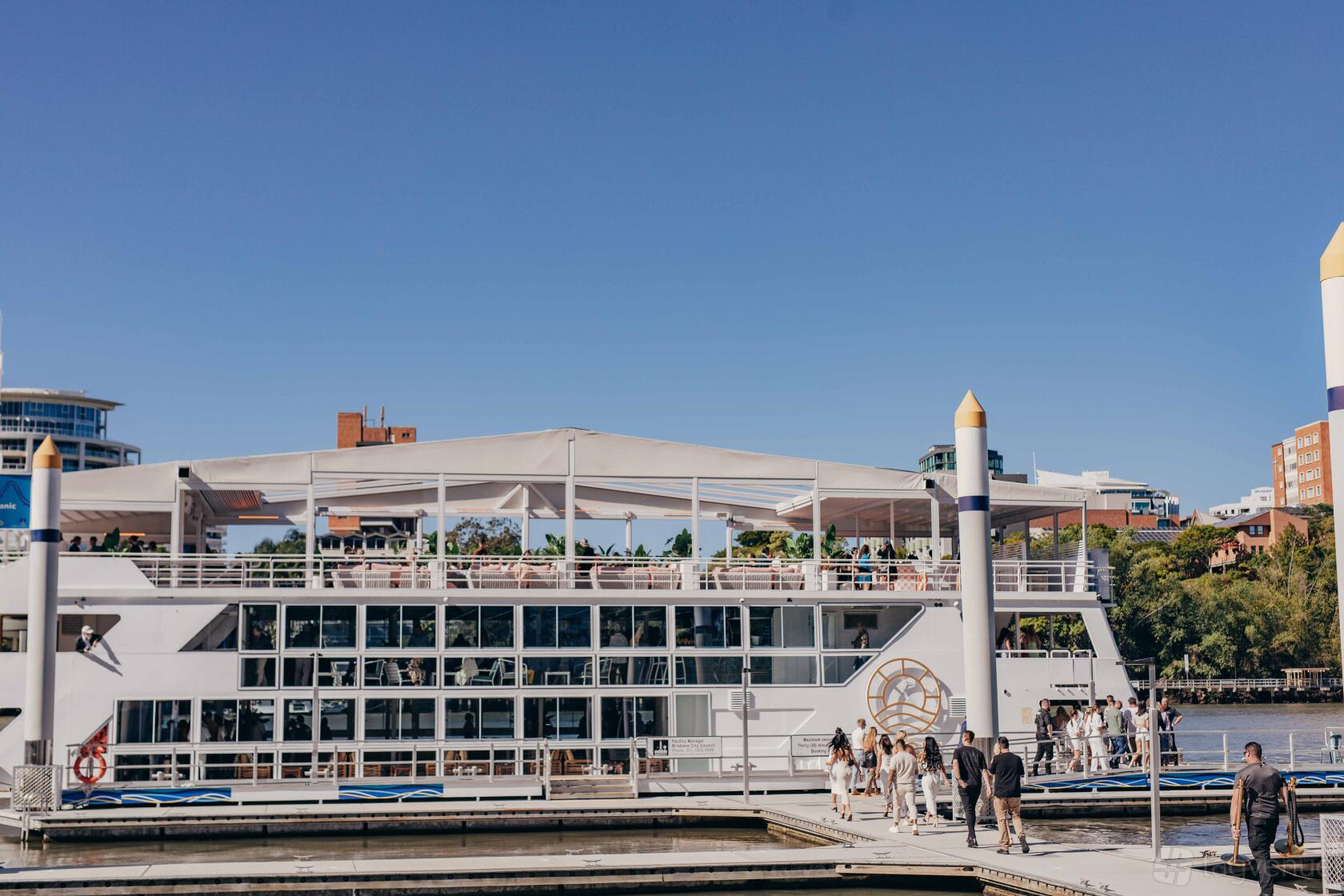 A boat with an open-air upper deck, white railings, and guests boarding at OASIS Brisbane.