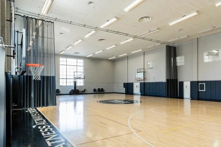 A sports hall with a polished wood basketball court, wall-mounted hoops, and high windows at JEM Community Center.