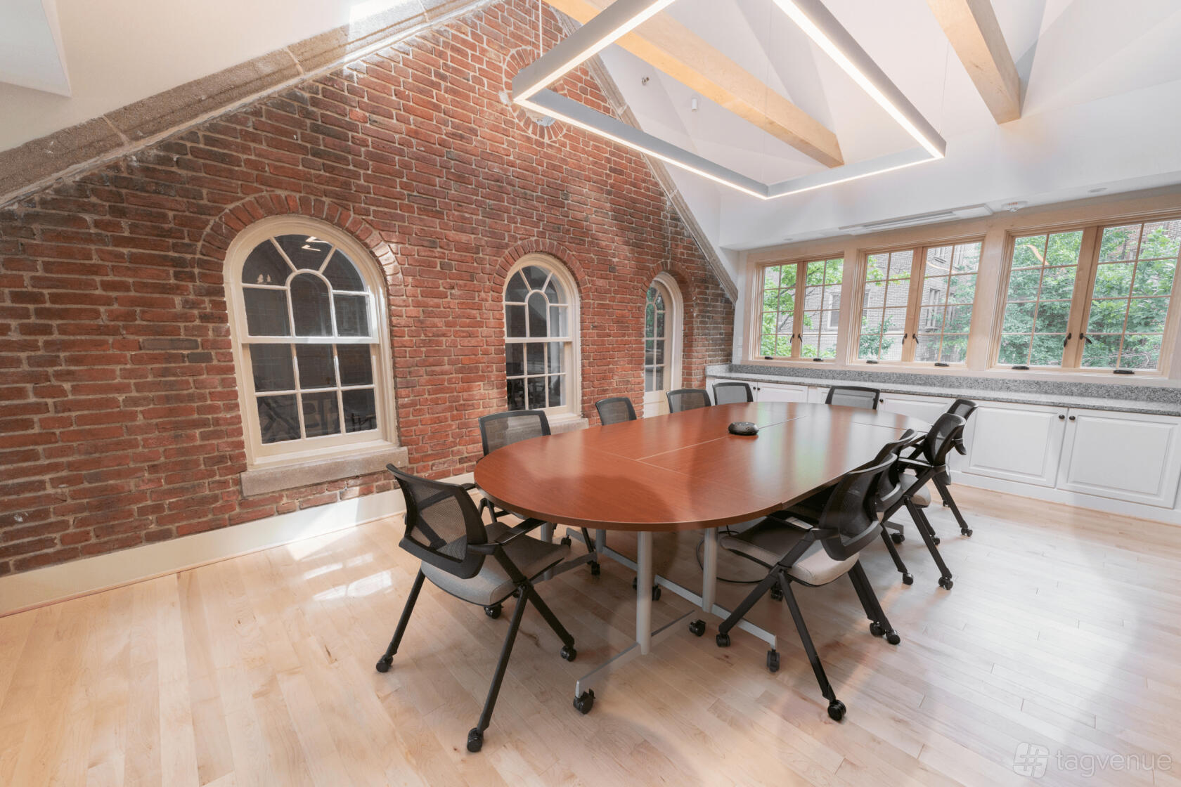 A boardroom with an oval wooden table, exposed brick walls, arched windows, and wooden ceiling beams at Friends Meeting of Washington.