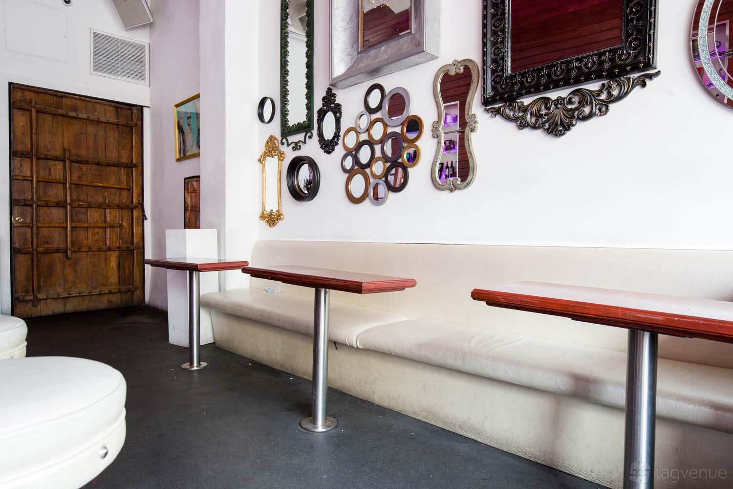 A function room with a long white banquette, wood tables, and an eclectic wall of decorative mirrors at Saint Felix Hollywood.