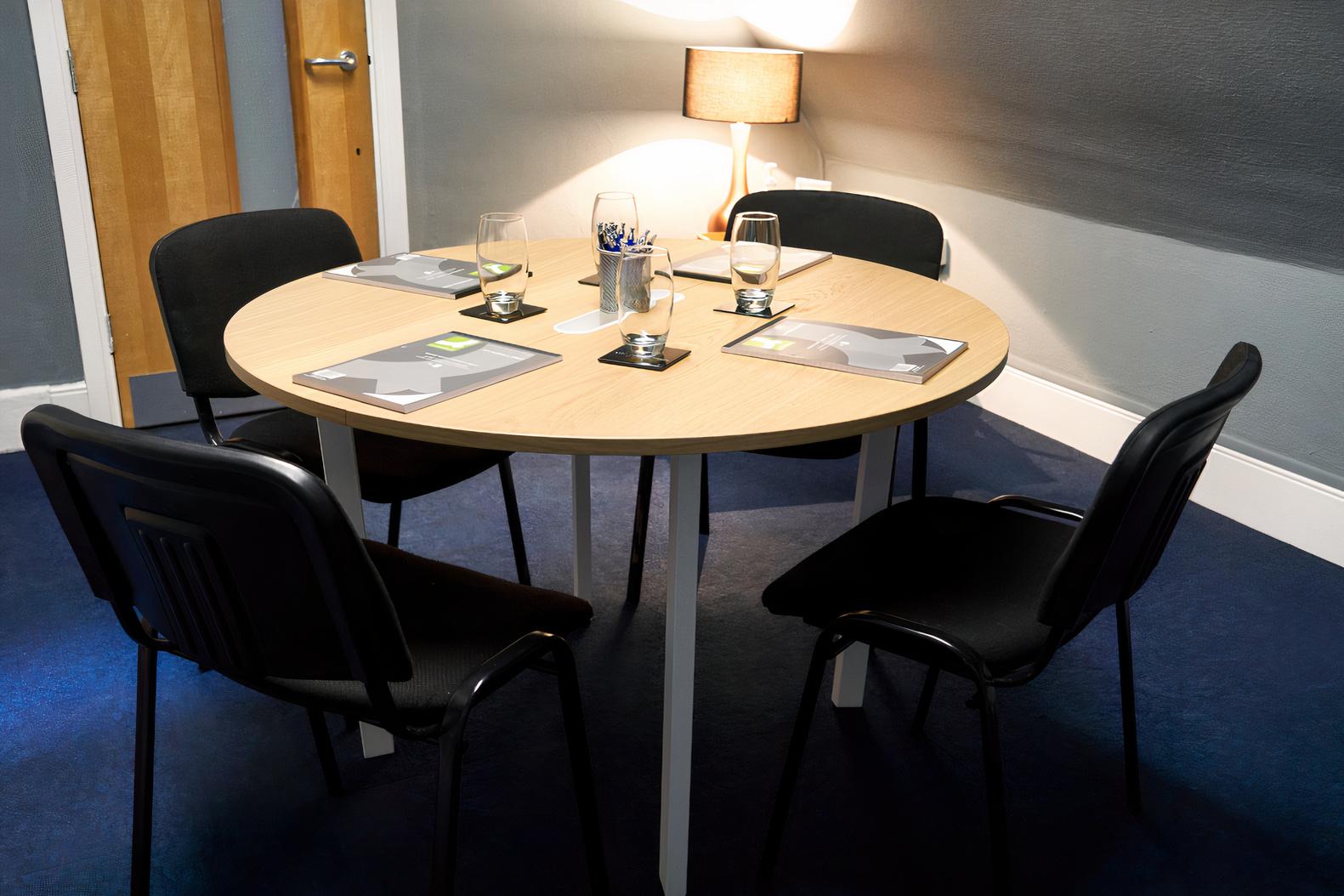 A meeting room with a round table, four black chairs, notepads, and a lamp at Clavering House.