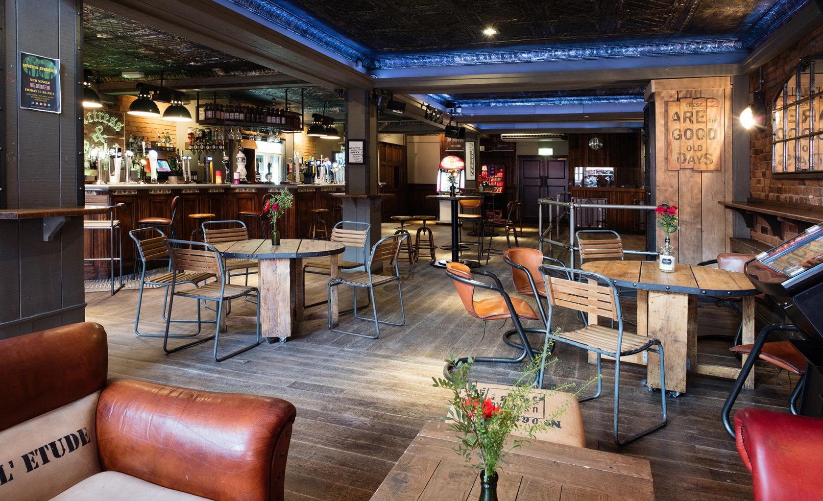An event space in a bar with exposed brick walls, wooden tables, metal chairs, and ambient lighting at The Actress & Bishop.