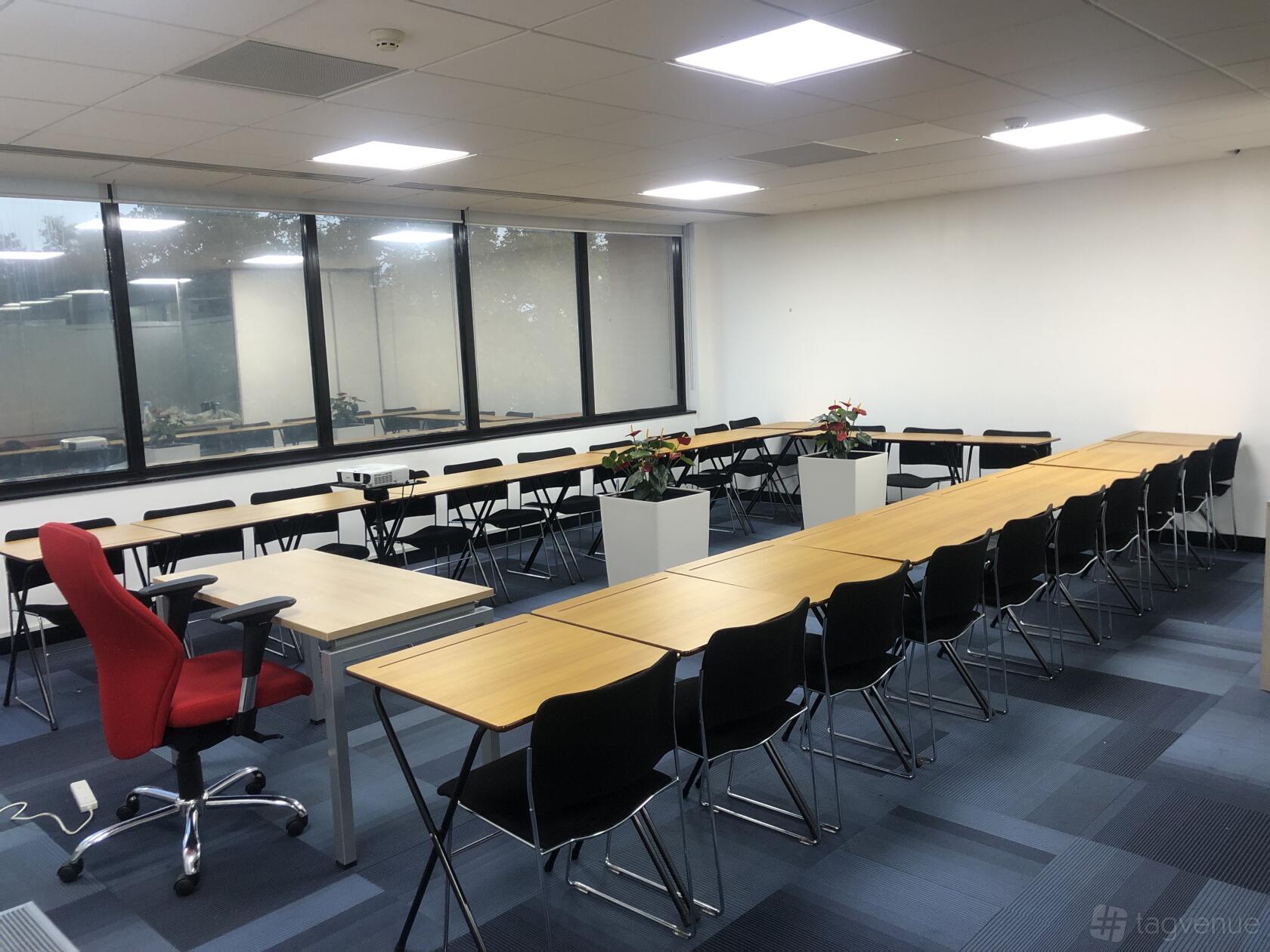 A conference centre with U-shaped tables, black chairs, large windows, and potted plants at Stratford.