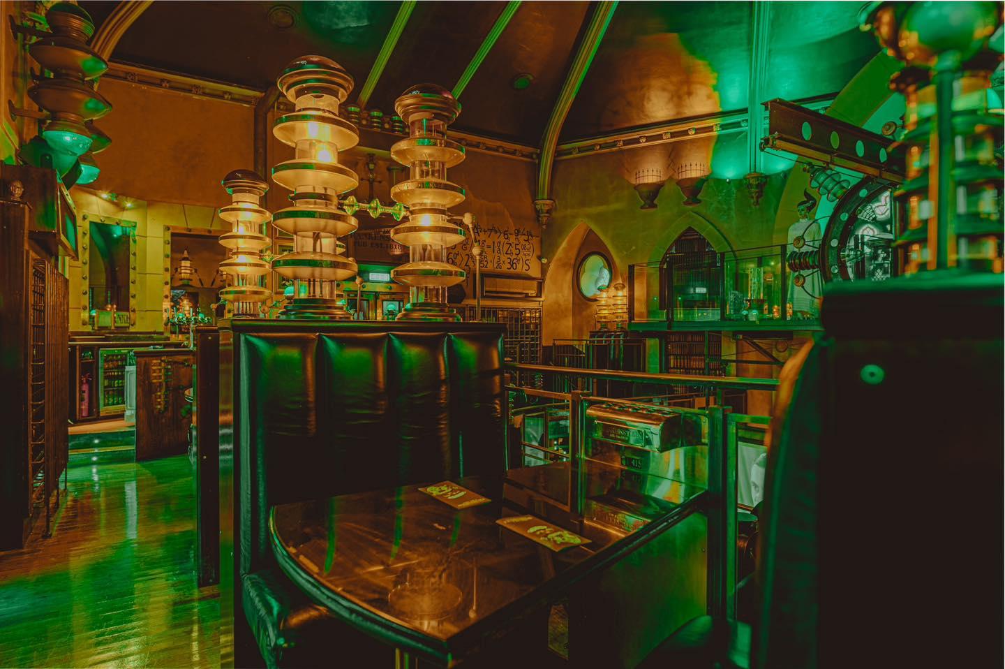 An event space in a pub with green lighting, high-backed booths, and gothic arches at Frankenstein's Edinburgh.