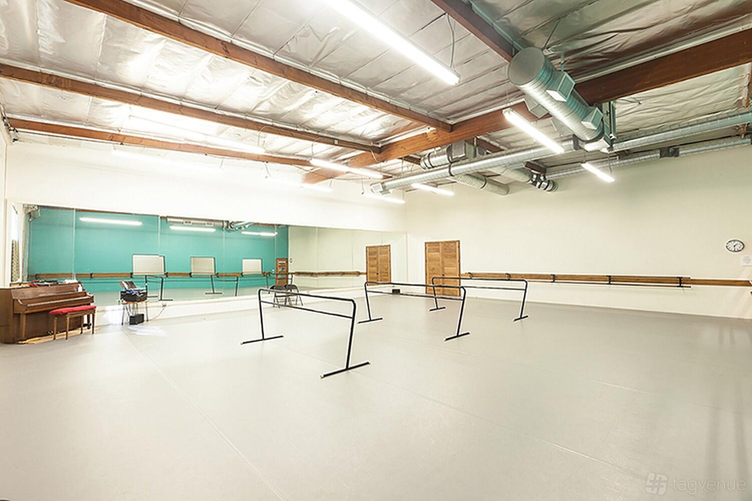 A dance studio with mirrored walls, ballet barres, overhead fluorescent lighting, and portable dance rails at California Dance Academy.
