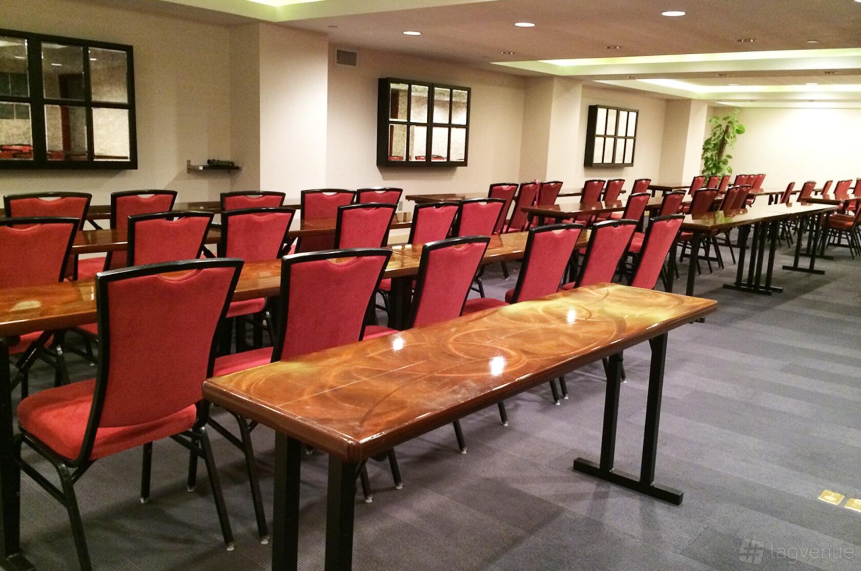 An event space with rows of wooden tables and red chairs in a carpeted room at Tryp New York City Times Square South.