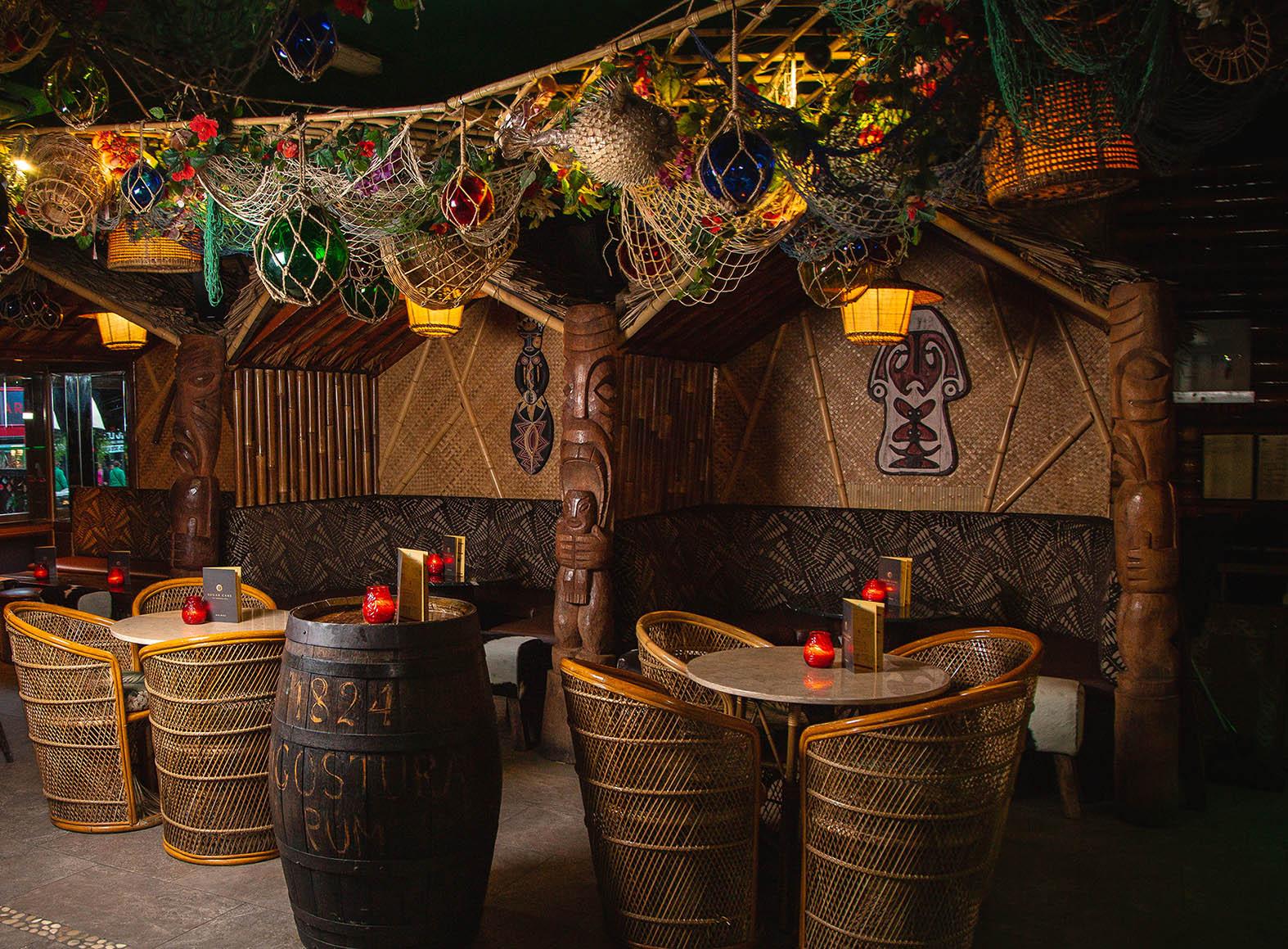 An event space in a cocktail bar with bamboo walls, tiki carvings, rattan chairs, and hanging lanterns at Sugar Cane.
