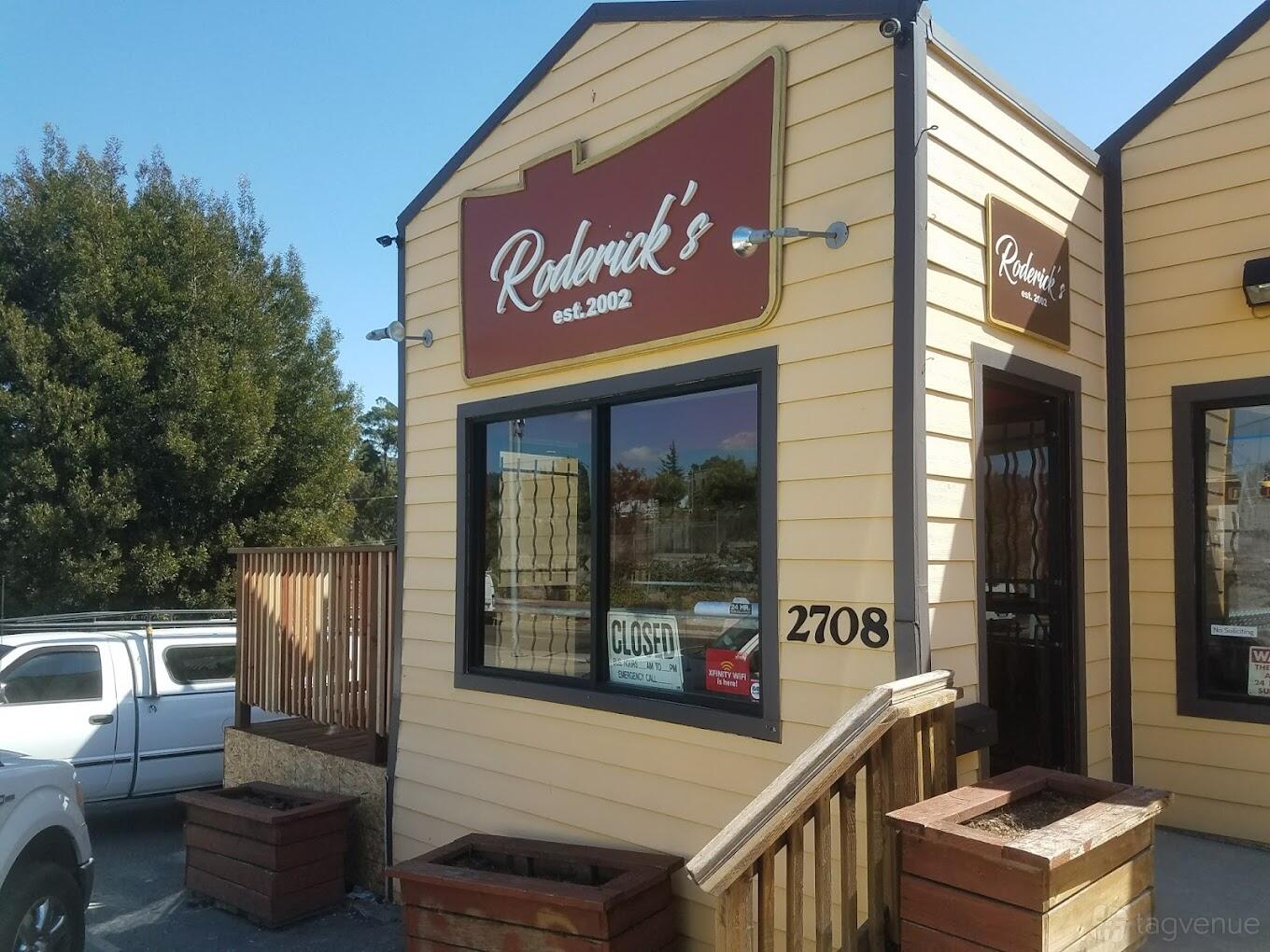 A restaurant with tan wooden siding, red signage, and a small entrance porch at Roderick's BBQ.