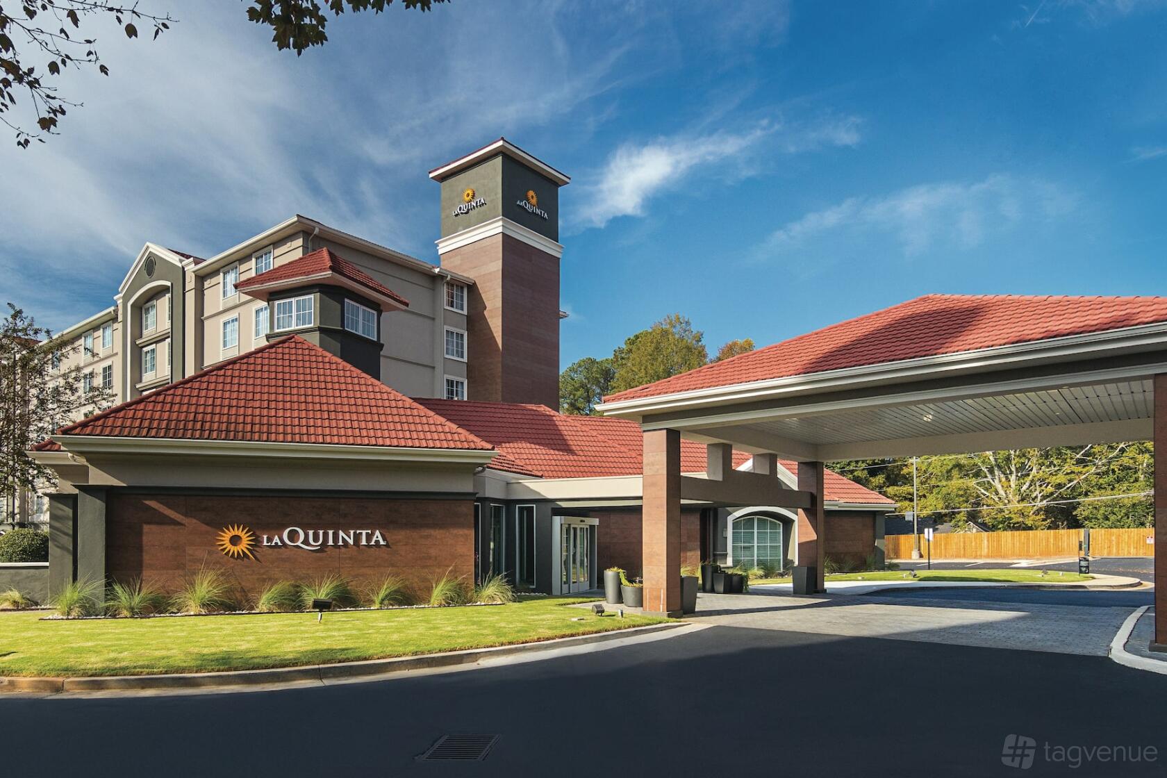 A hotel exterior with a red tiled roof, entrance porte-cochère, and landscaped grounds at La Quinta Inn & Suites Atlanta Conyers.