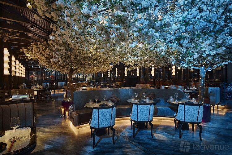 An event space in a restaurant with cherry blossom ceiling décor, blue lighting, and round tables at TATTU London.