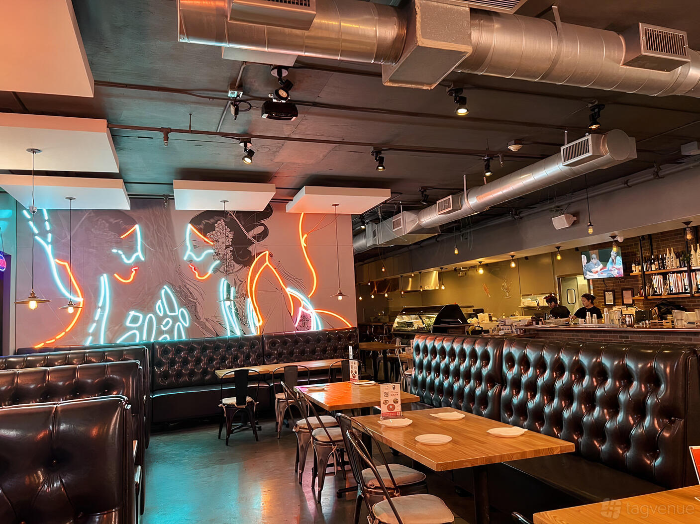 A restaurant with tufted leather banquettes, wooden tables, and neon wall art at Tang Dynasty.