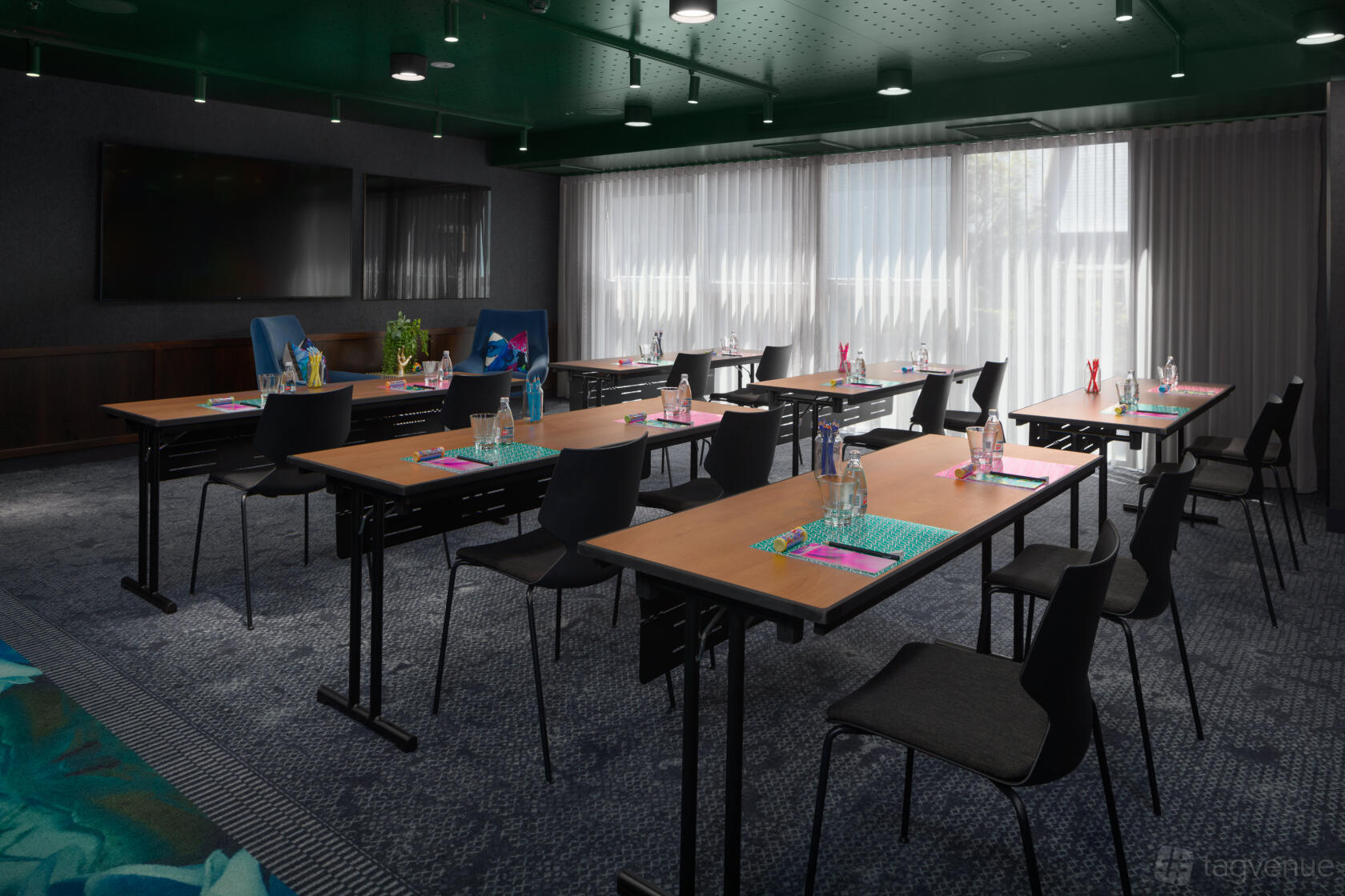 An event space in a hotel with floor-to-ceiling sheer curtains, individual desks, and bottled water at Zagame's House.