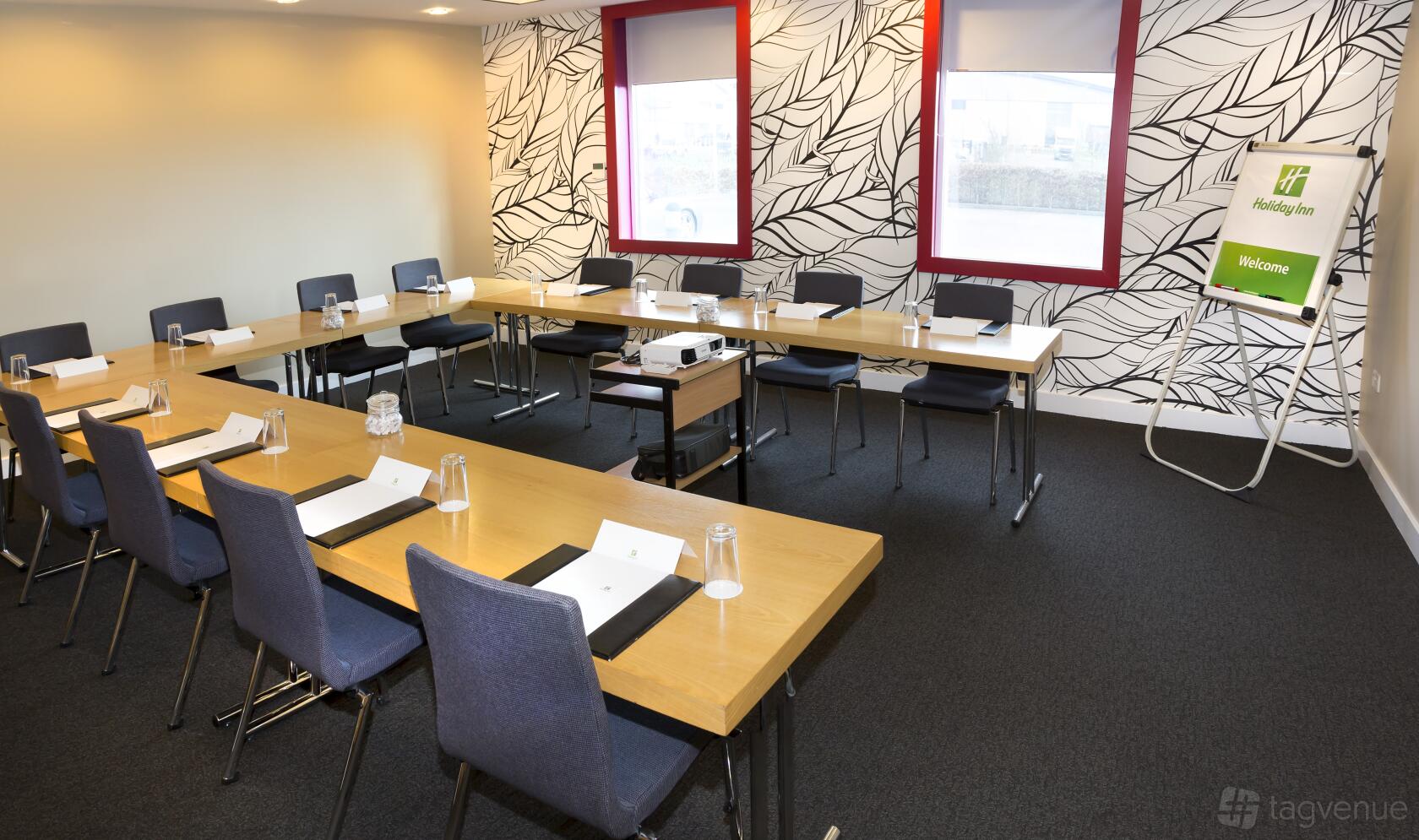 A hotel meeting room with U-shaped tables, navy chairs, notepads, and patterned wall at Holiday Inn Salisbury-Stonehenge.