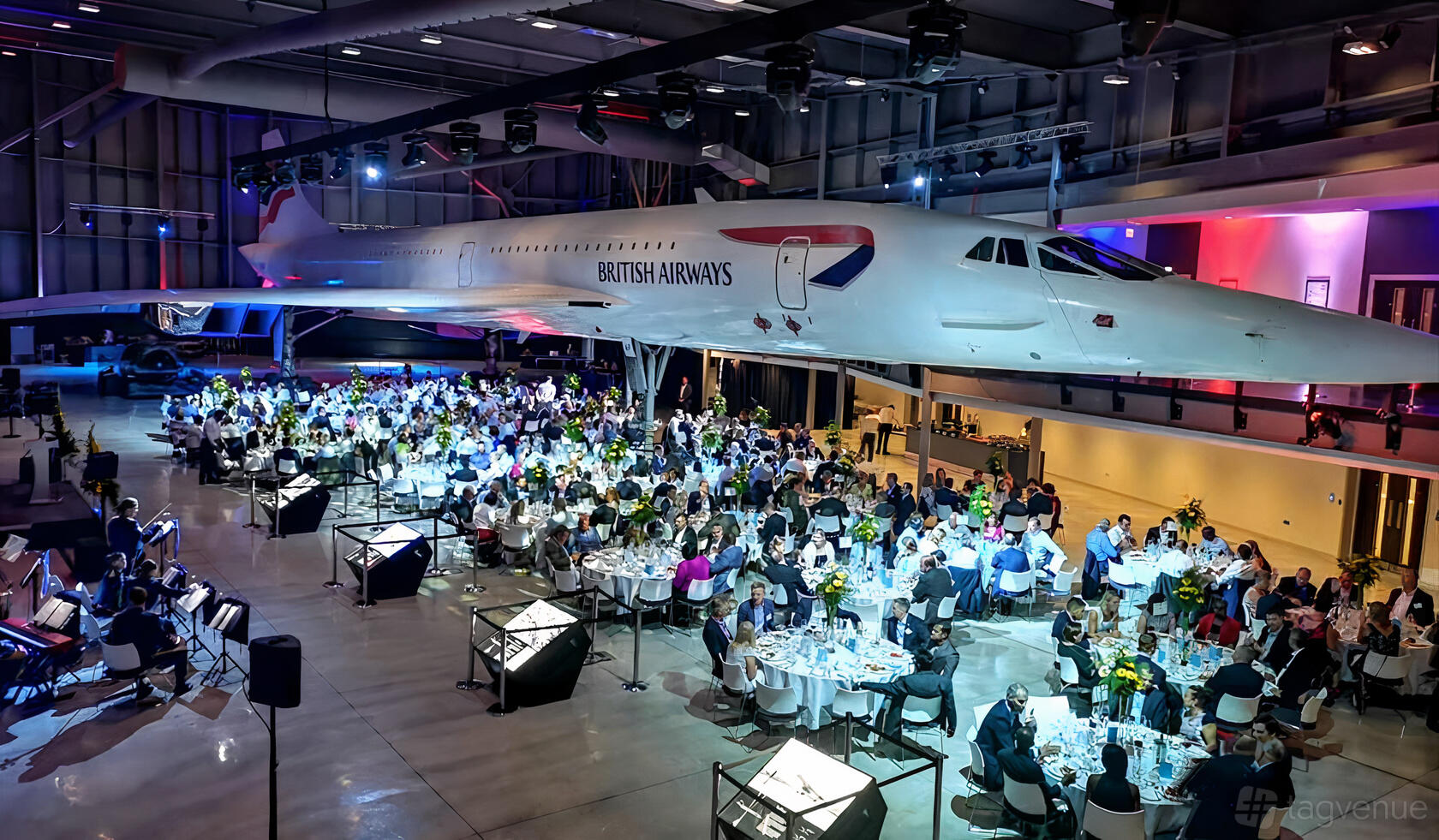 A museum gallery with banquet tables set beneath a suspended Concorde aircraft at Aerospace Bristol.