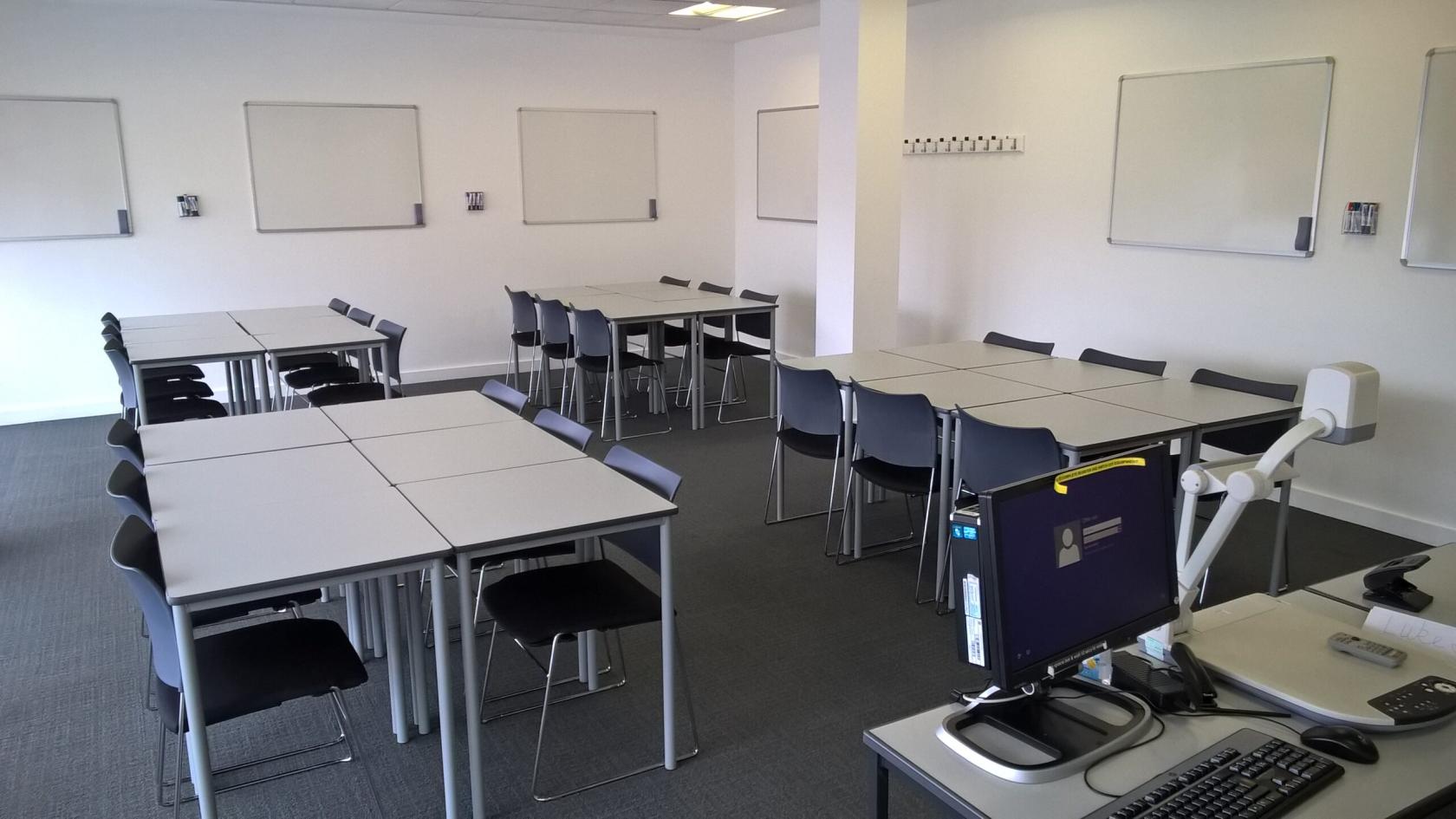 A meeting room with modular tables, black chairs, whiteboards, and a projector at The University of Law - Manchester Campus.