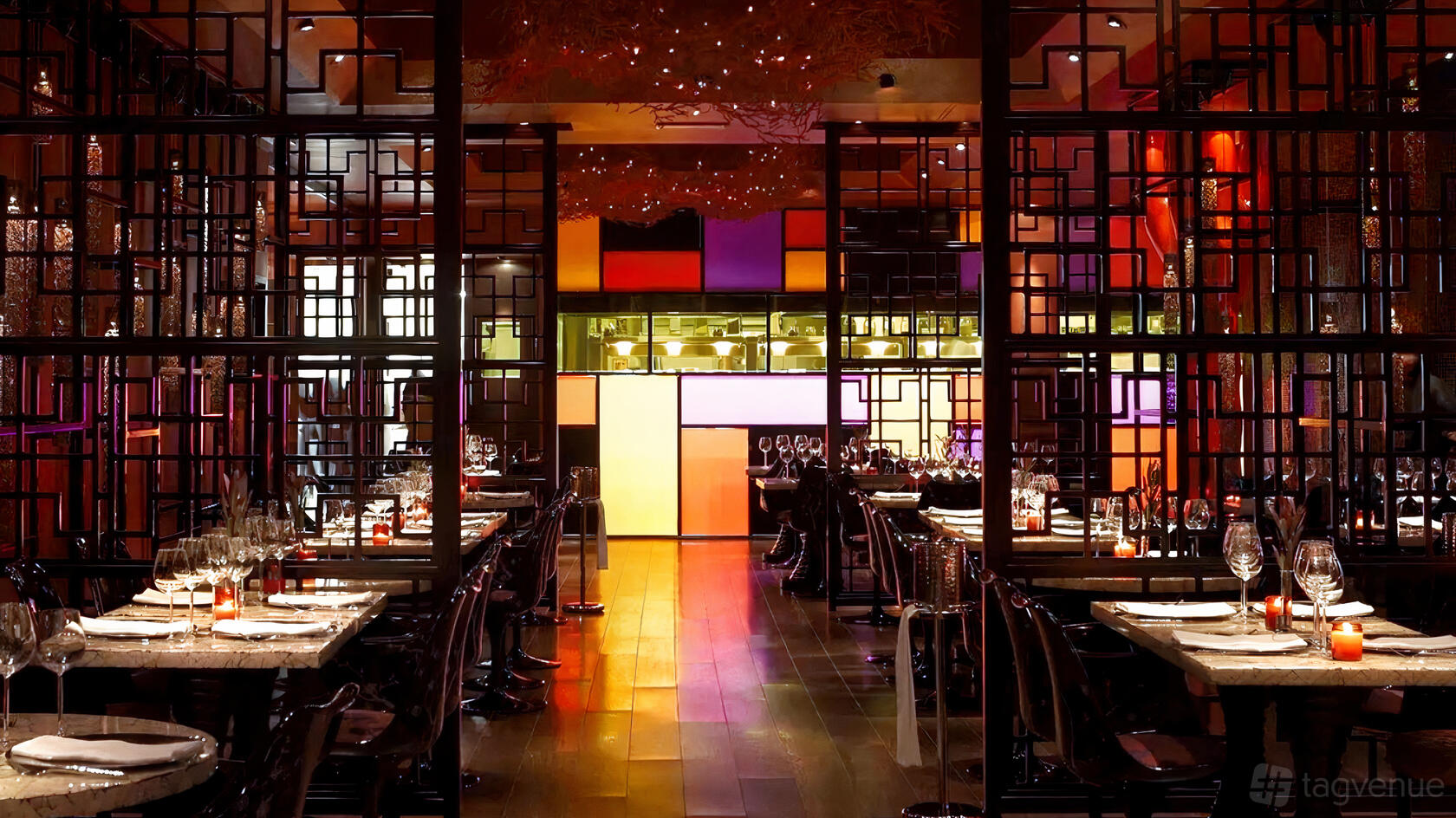 A restaurant with decorative wood lattice dividers, long set tables, and colorful backlit panels at Vermilion.