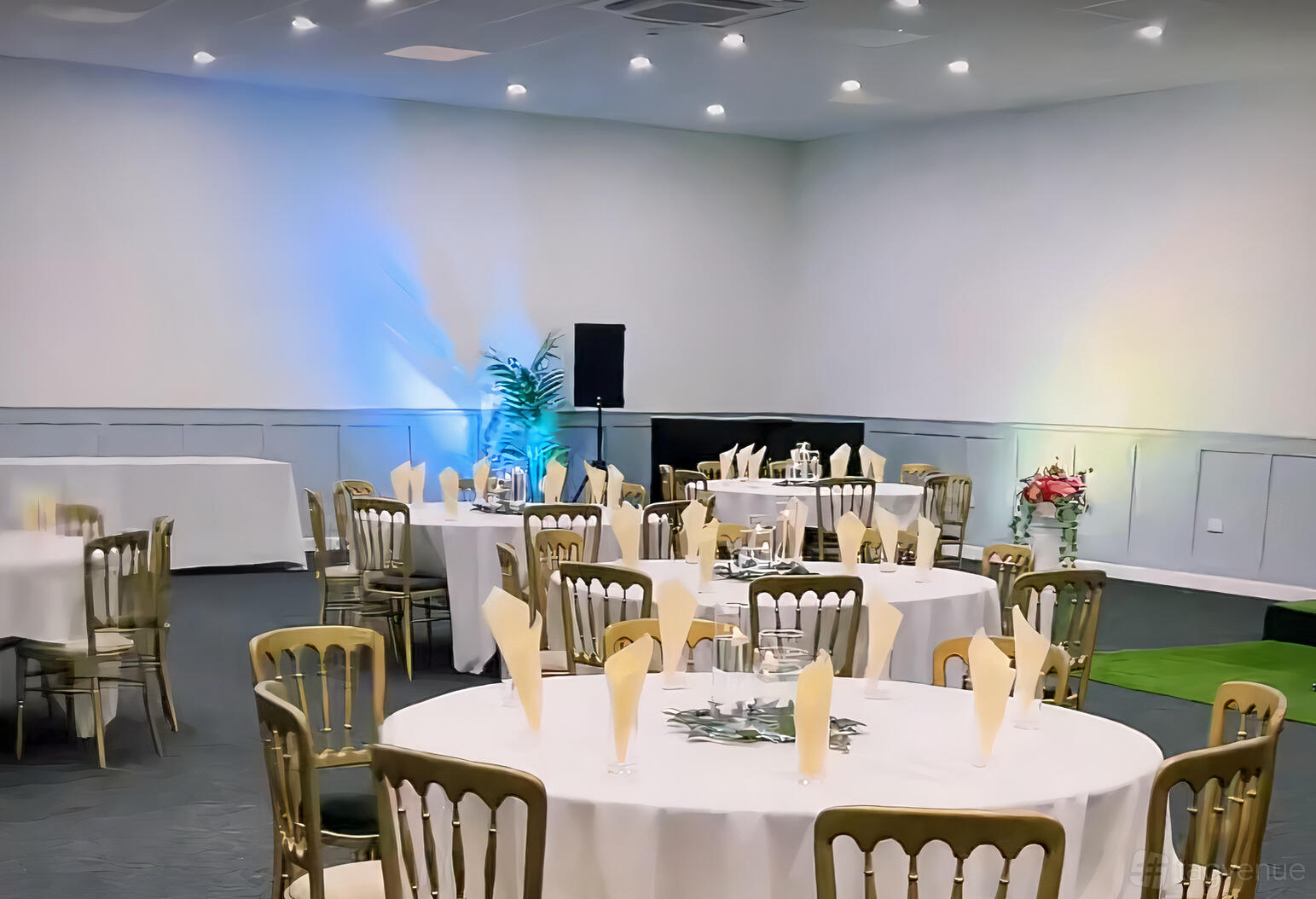 A banquet hall with round tables, gold chairs, napkin place settings, and colorful uplighting at No.4 Banqueting & Events Hall.