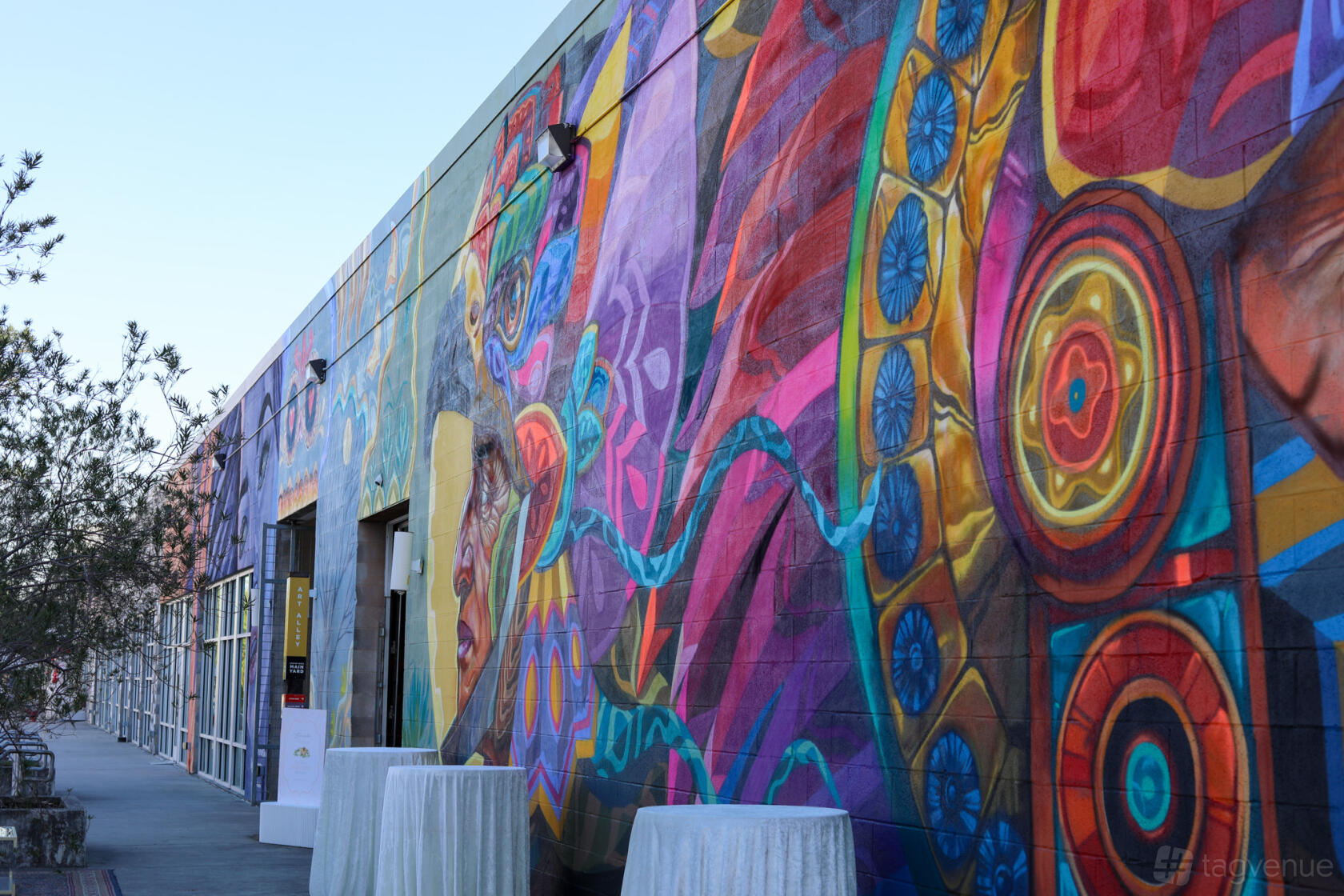 An event venue with a colorful mural-covered exterior wall and cocktail tables draped in white linens at Sawyer Station HTX.