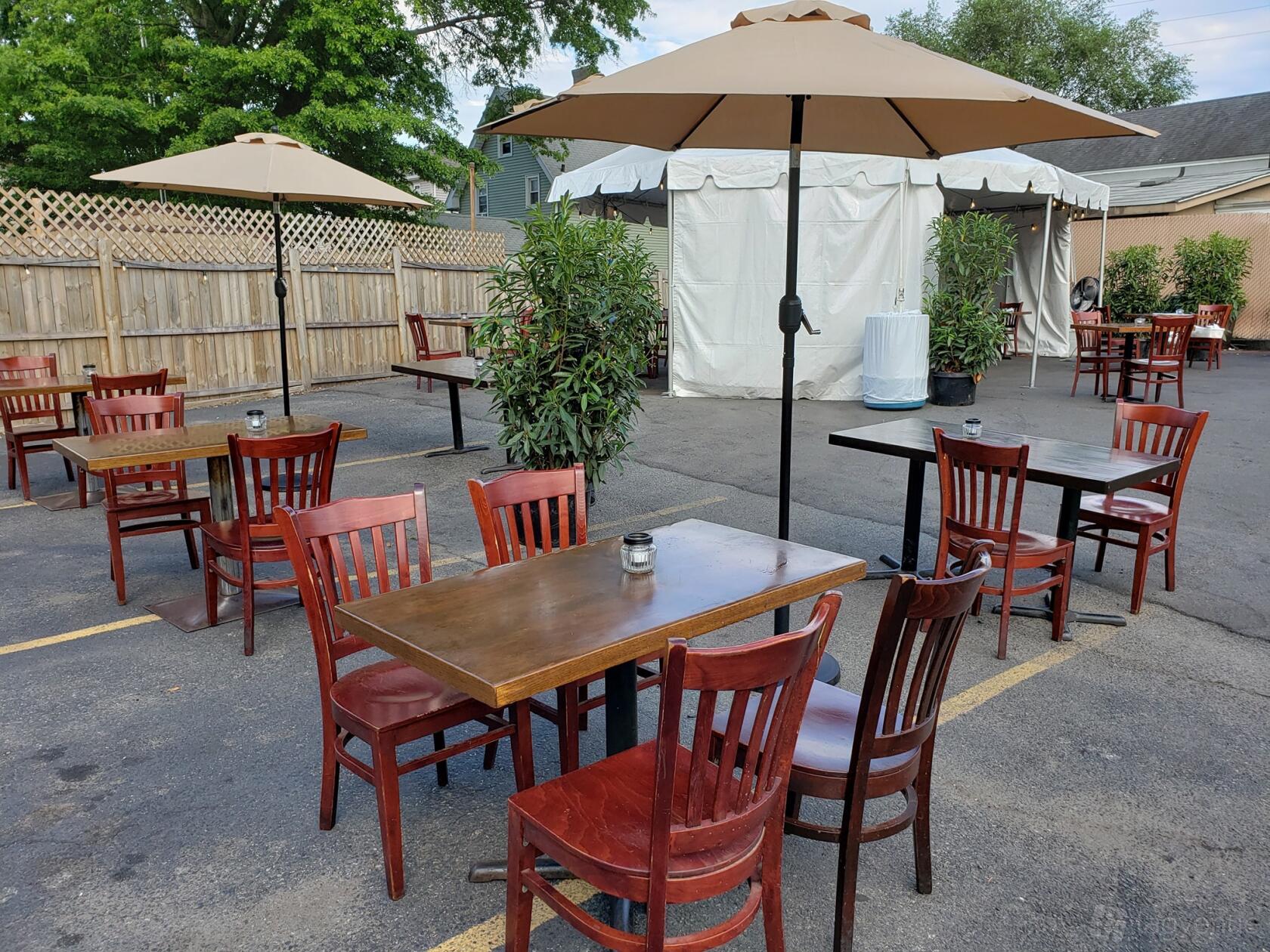An outdoor terrace with wooden tables, red chairs, large umbrellas, and potted plants at West Shore Inn.