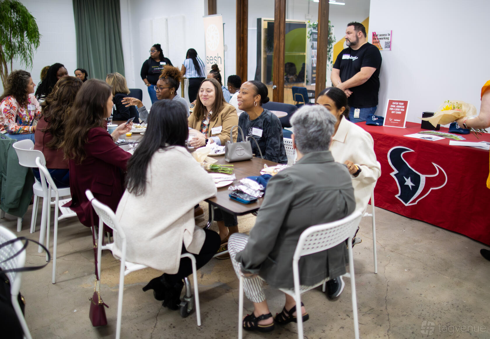 An event space with groups seated at tables, concrete floors, and a kitchenette area at Sesh Coworking.