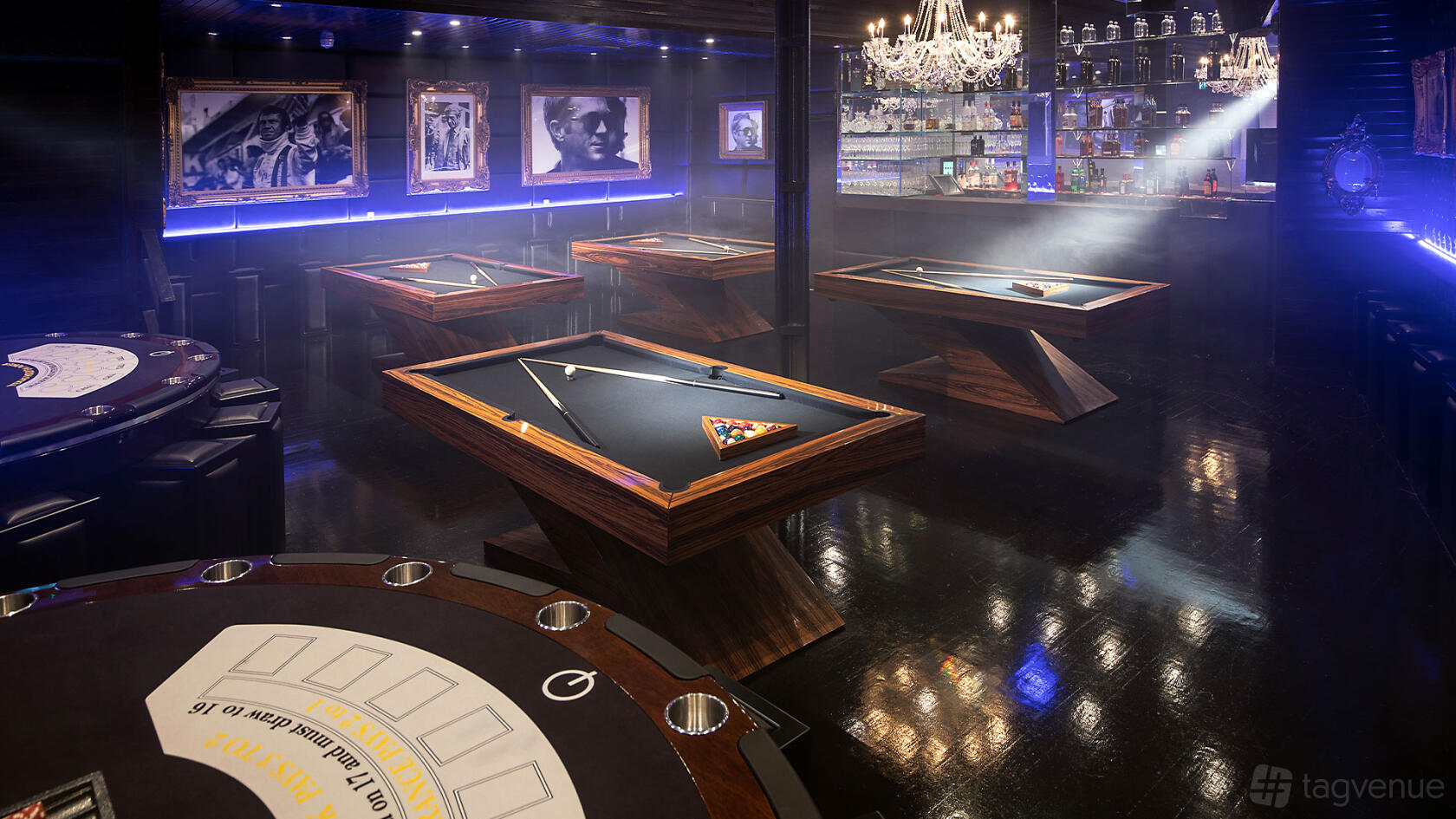 A cocktail bar with pool tables, chandeliers, framed photos, and a backlit bar counter at Q Shoreditch.