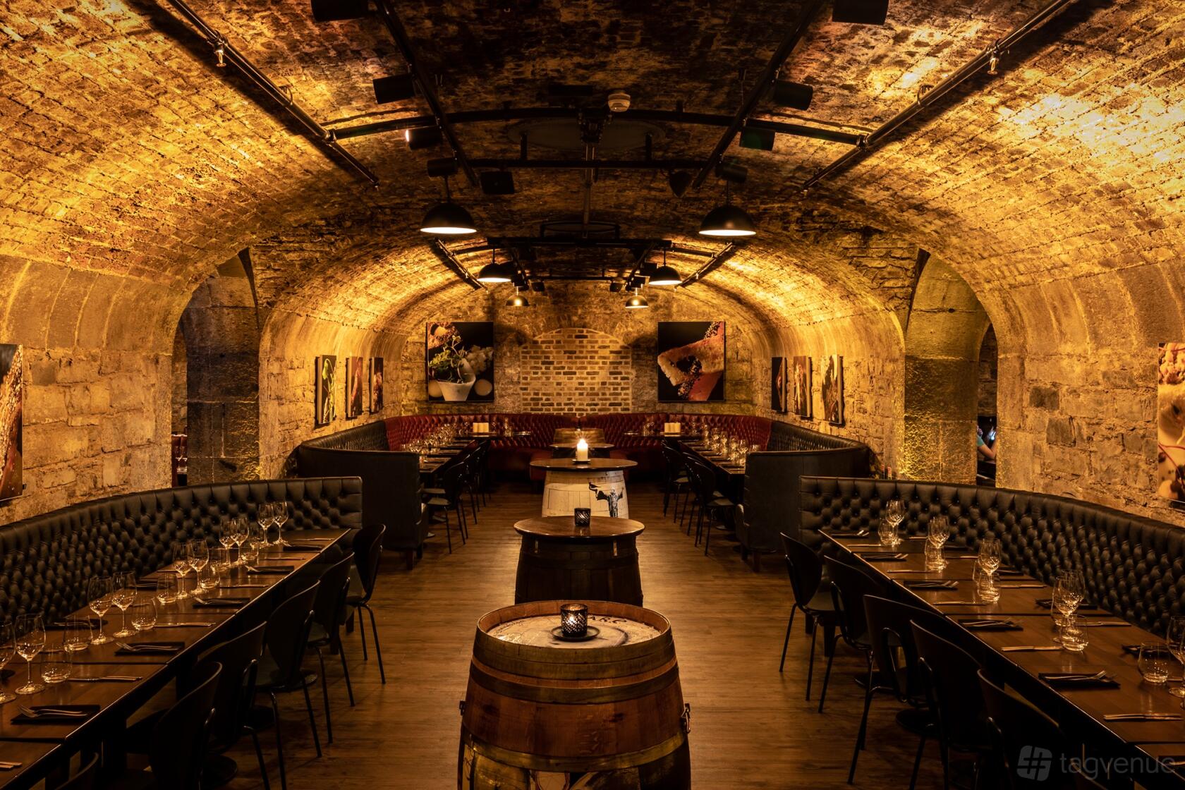 An event space with arched brick ceilings, exposed stone walls, and long dining tables at Urban Brewing Vaults.