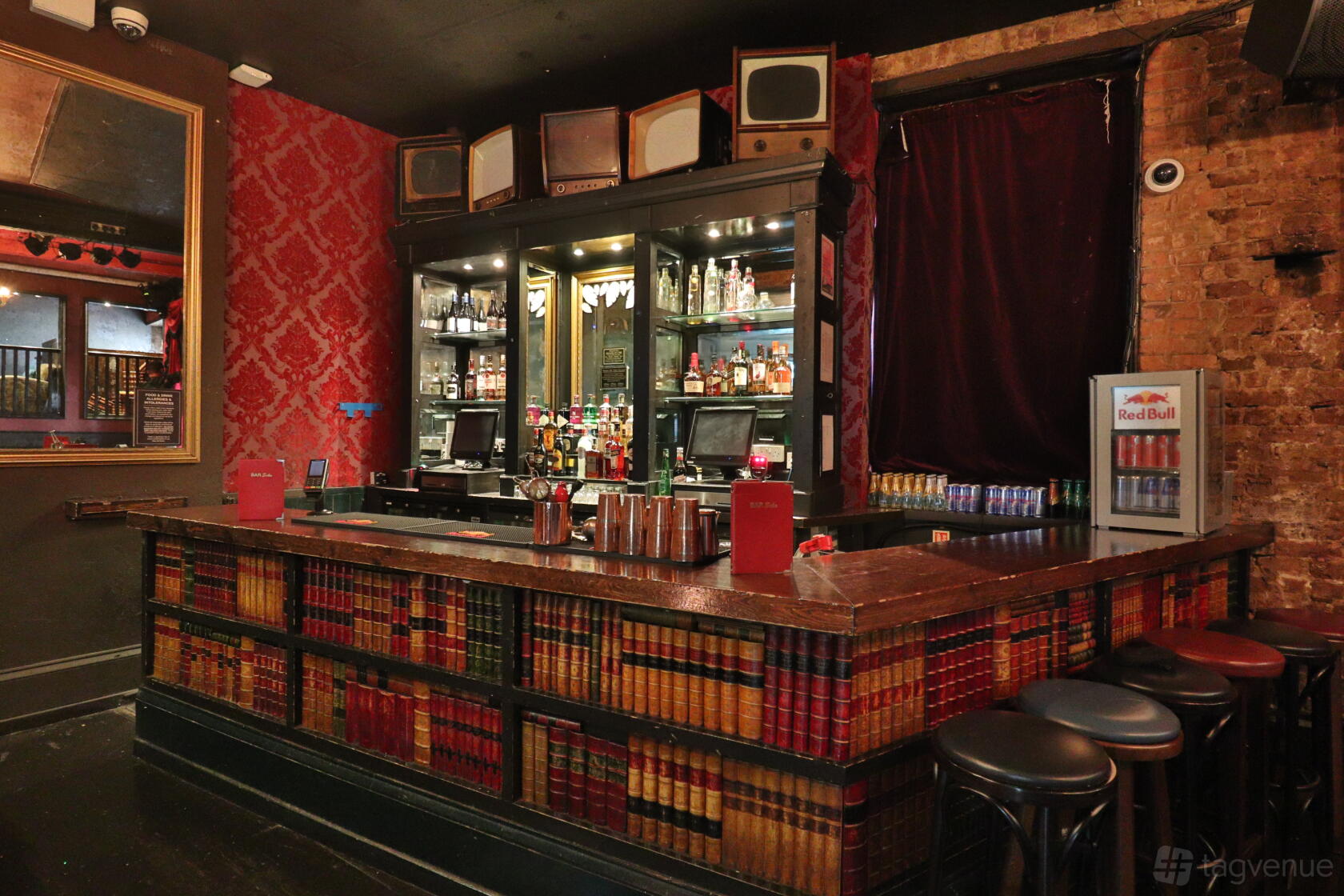An event space with vintage wallpaper, a mirrored bar, and bookshelves decorated with retro TVs at Bar Soho.