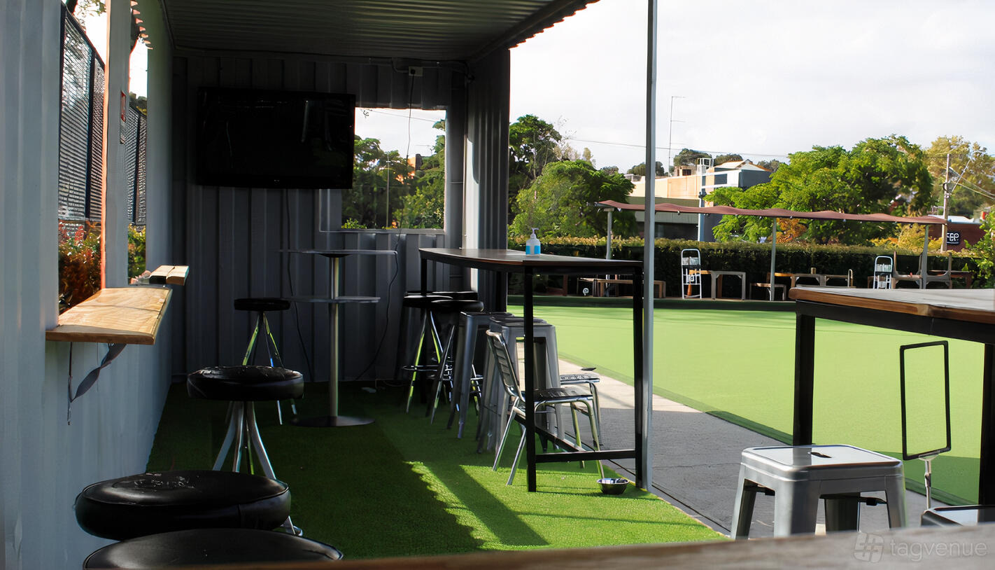 An outdoor event venue with tall tables, metal stools, and artificial lawn at Flemington and Kensington Bowling Club.