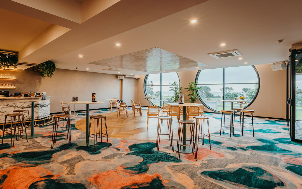 A hotel bar with round windows, colorful carpet, high-top tables, and a marble-topped counter at Rye Hotel.
